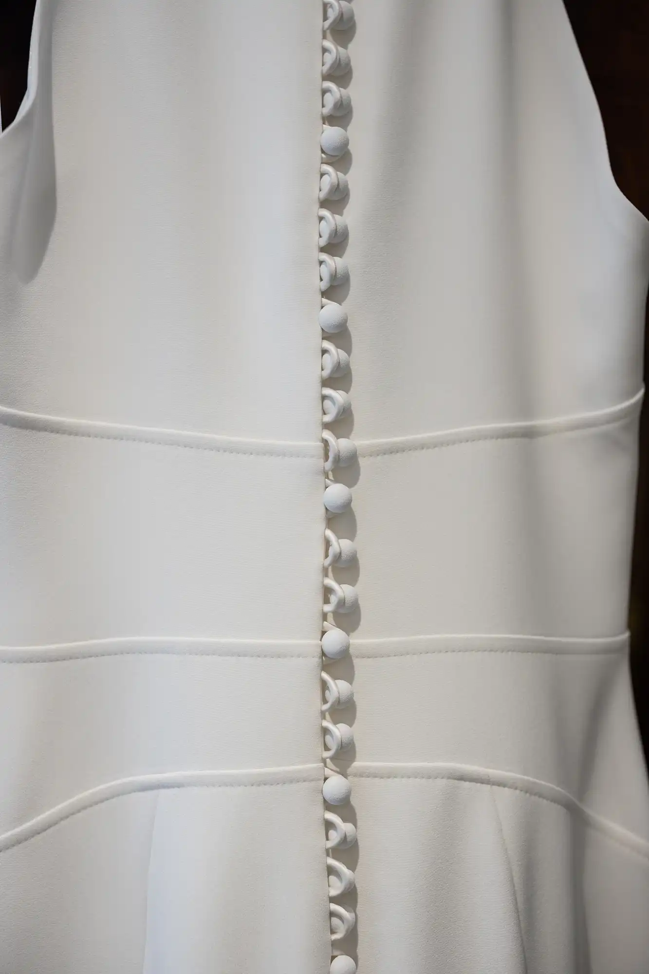 Close-up of a white garment with a detailed row of small, round buttons running vertically down the back.