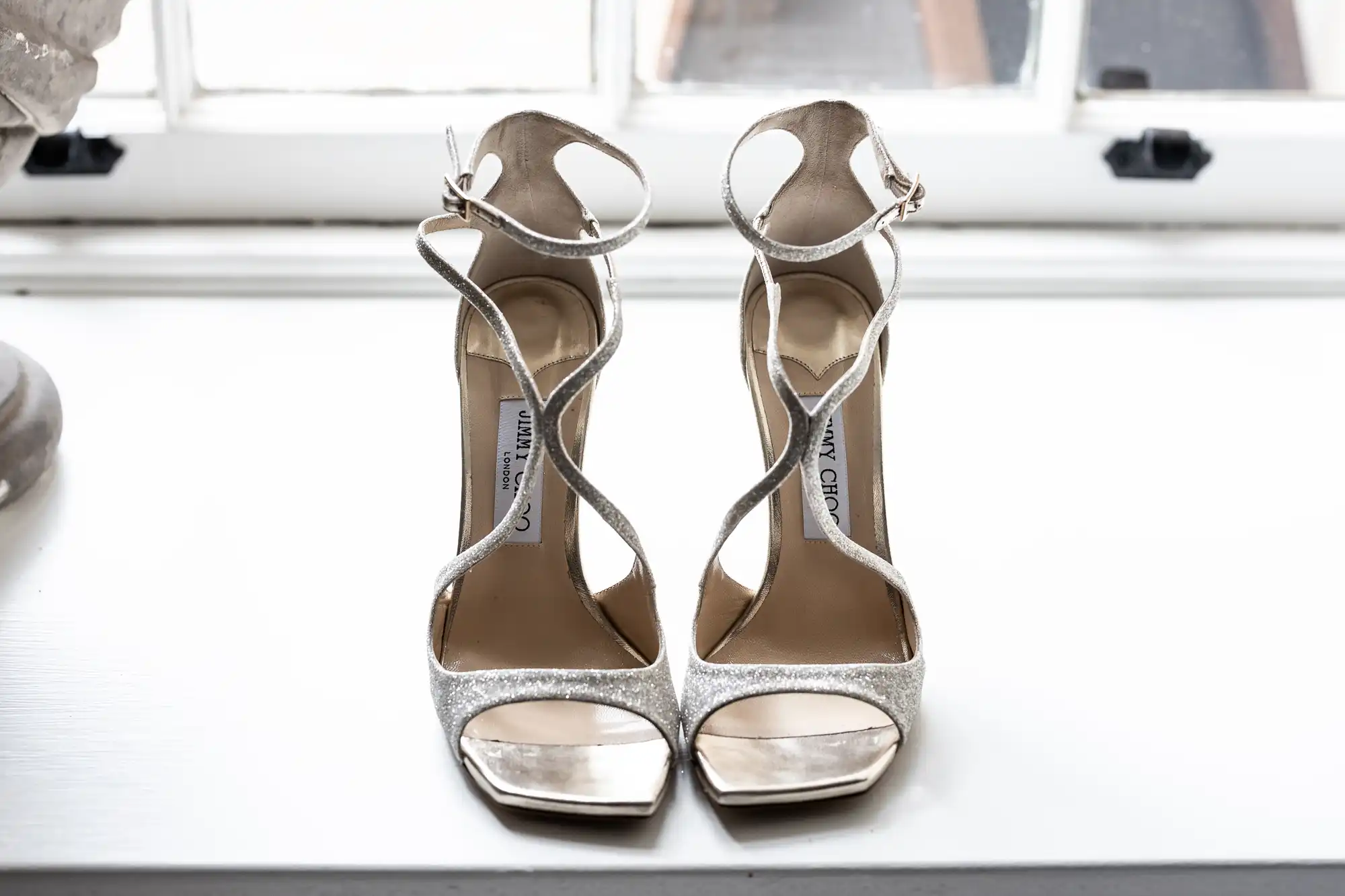 A pair of silver glitter high-heeled sandals placed neatly on a windowsill.