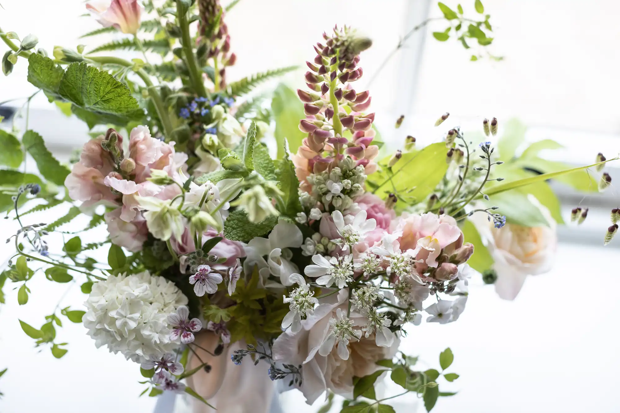 A close-up of a vibrant bouquet featuring various flowers including pink blossoms and lush greenery.