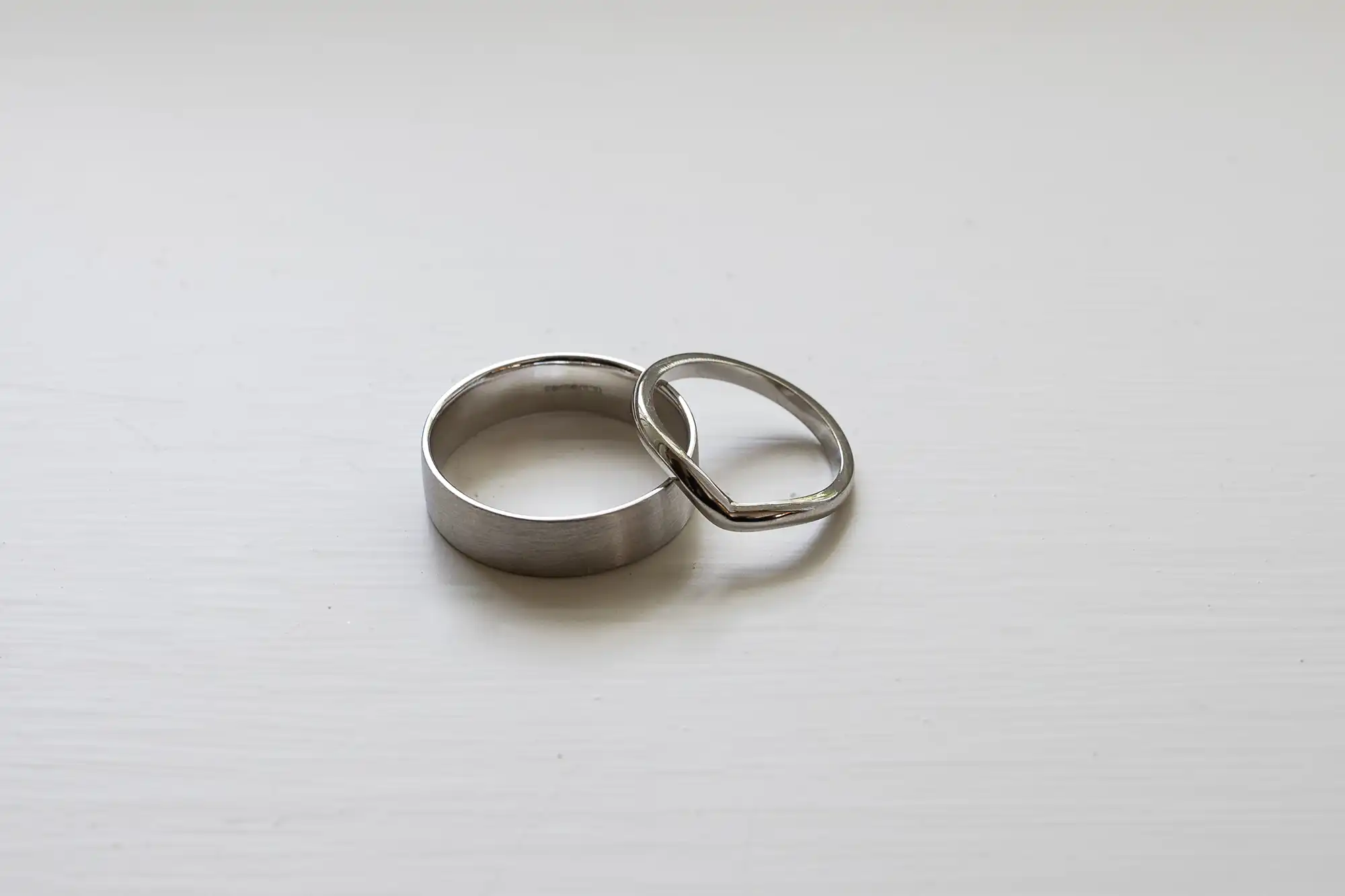 Two wedding rings, one with a classic band and the other with a twisted design, resting on a white surface.