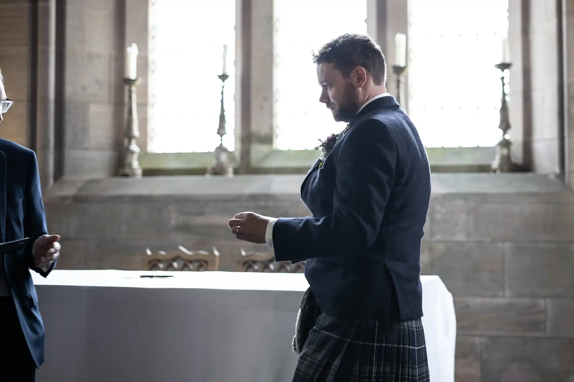A man in a kilt and jacket stands solemnly in a church, appearing to be part of a ceremony.