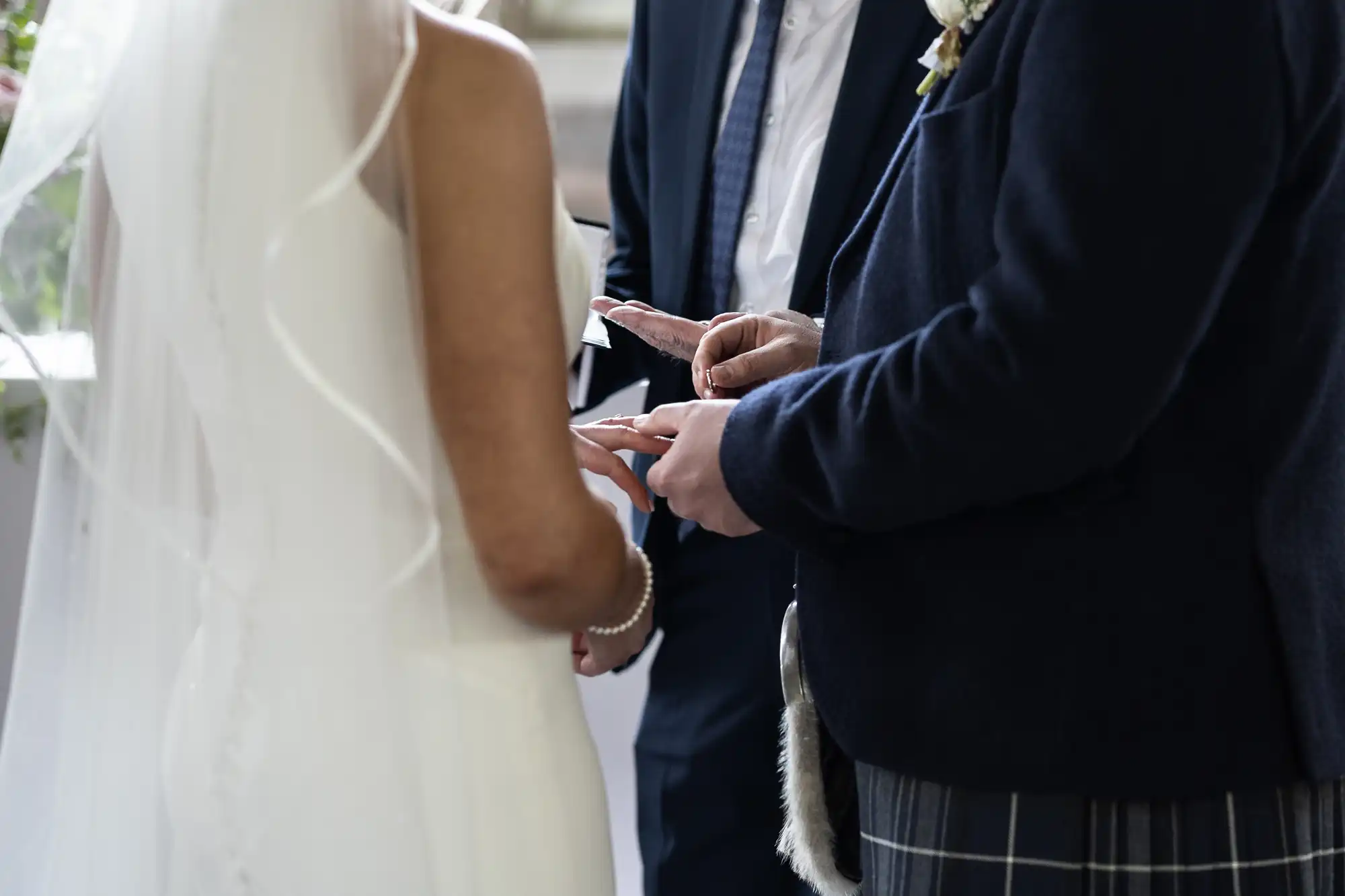 A bride and groom exchange rings during a wedding ceremony, with the groom wearing a kilt and the bride in a white gown.