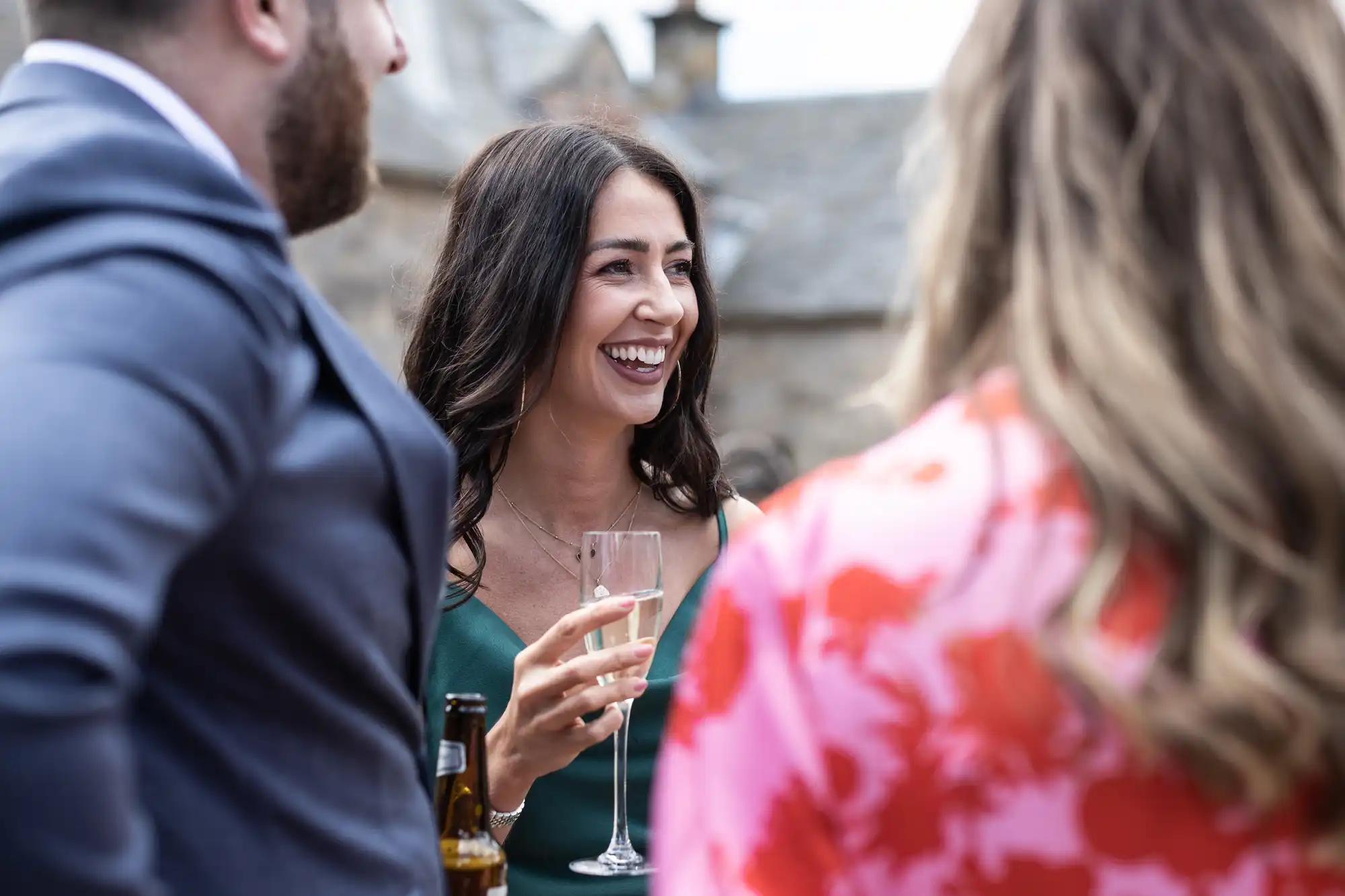 Woman in green dress laughing and holding a champagne glass at an outdoor social gathering.