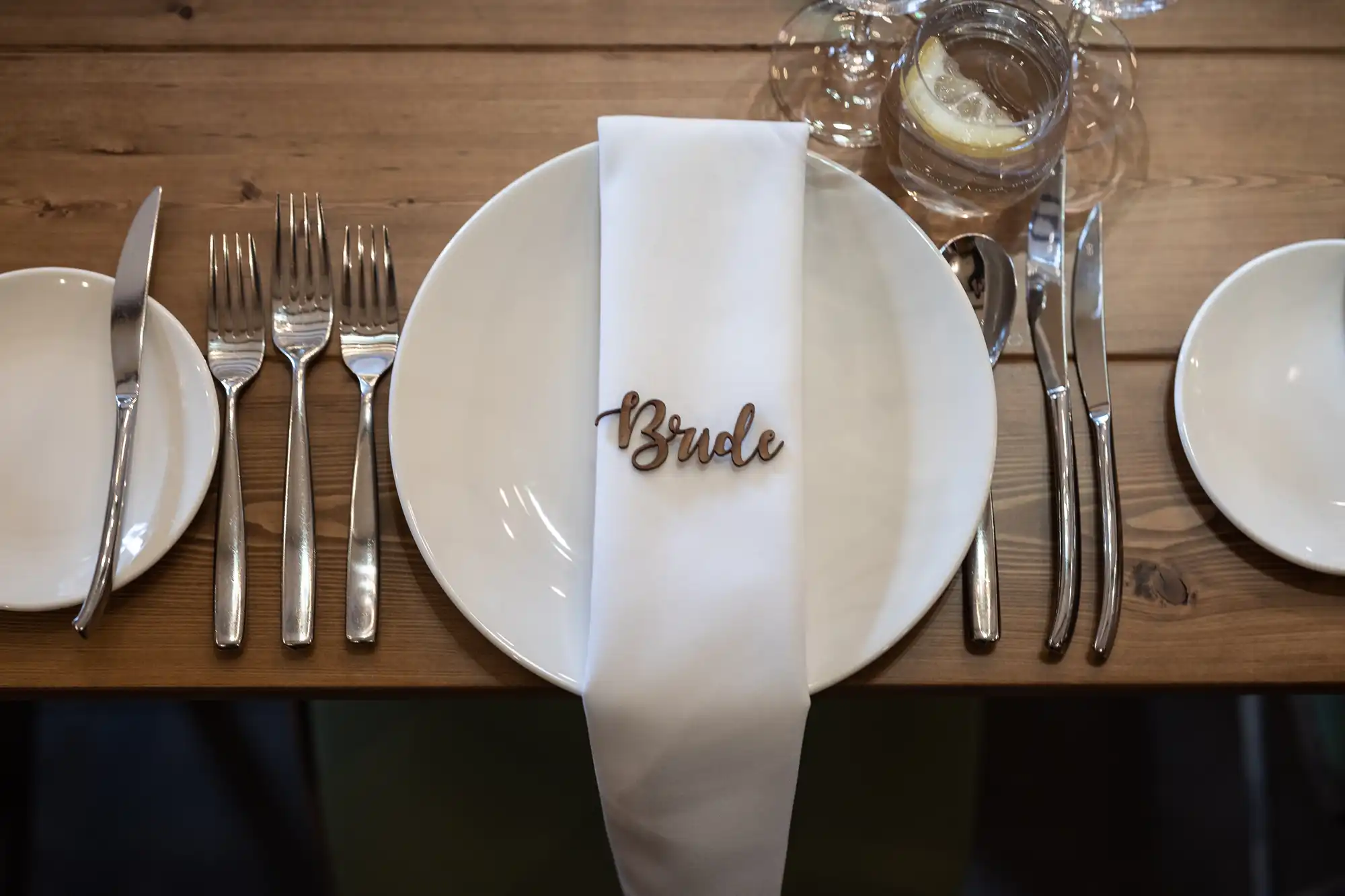 An elegant wedding table setting featuring a plate with a napkin embroidered with the word "Bride," surrounded by silverware and glasses.