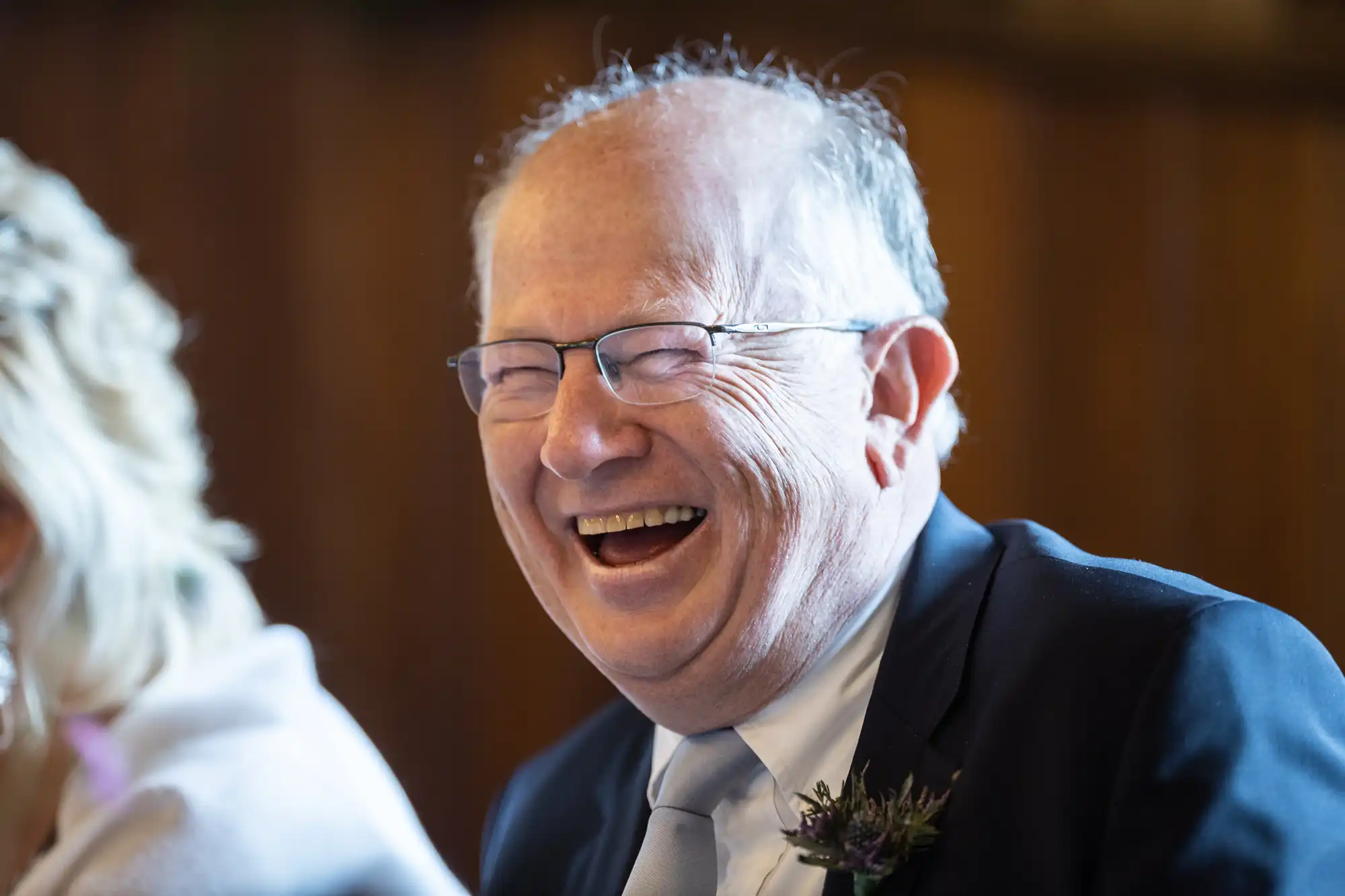 A man in a suit laughing heartily at a wedding reception.
