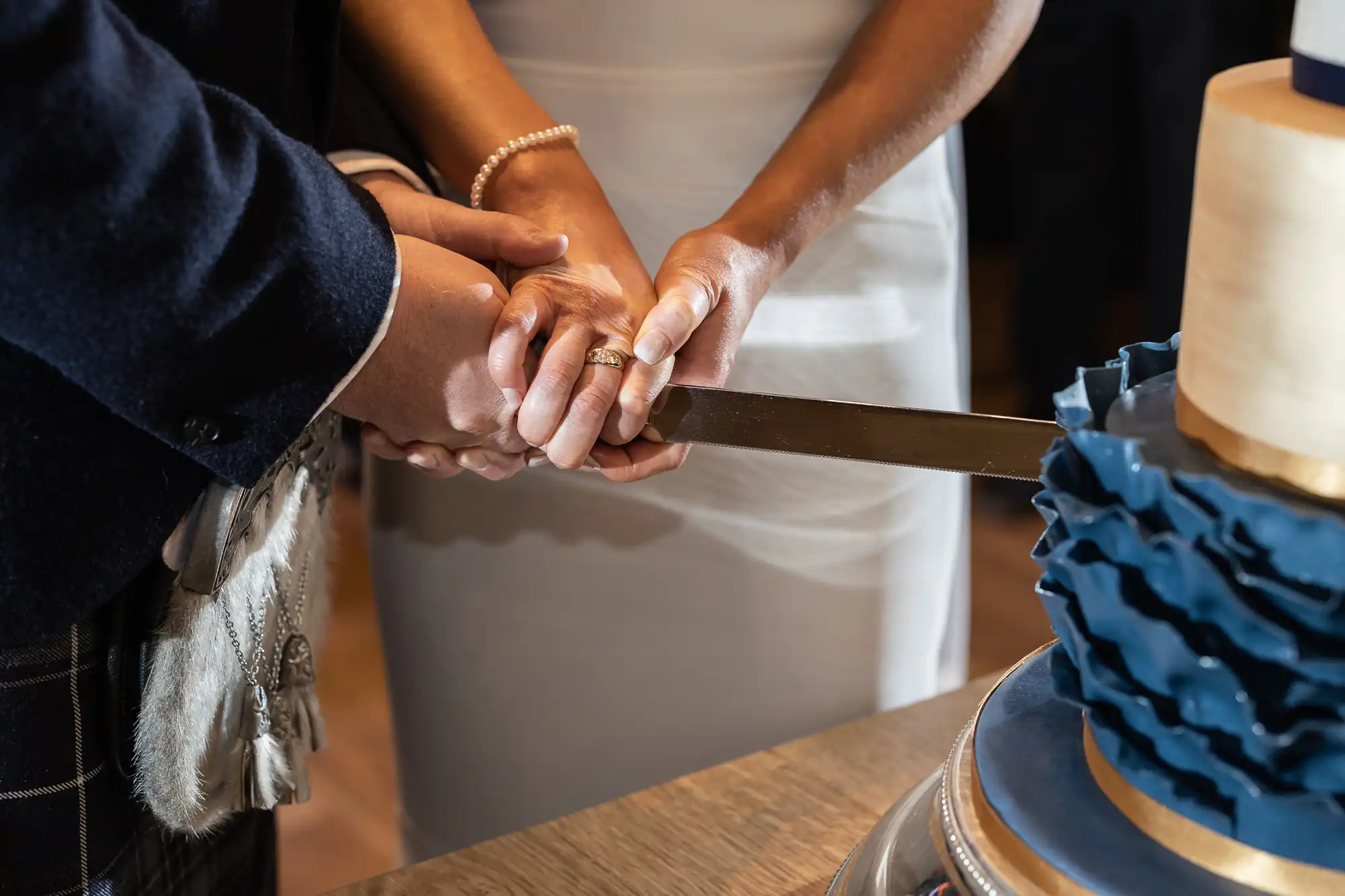 A newlywed couple in ceremonial attire cutting a multi-tiered wedding cake together.