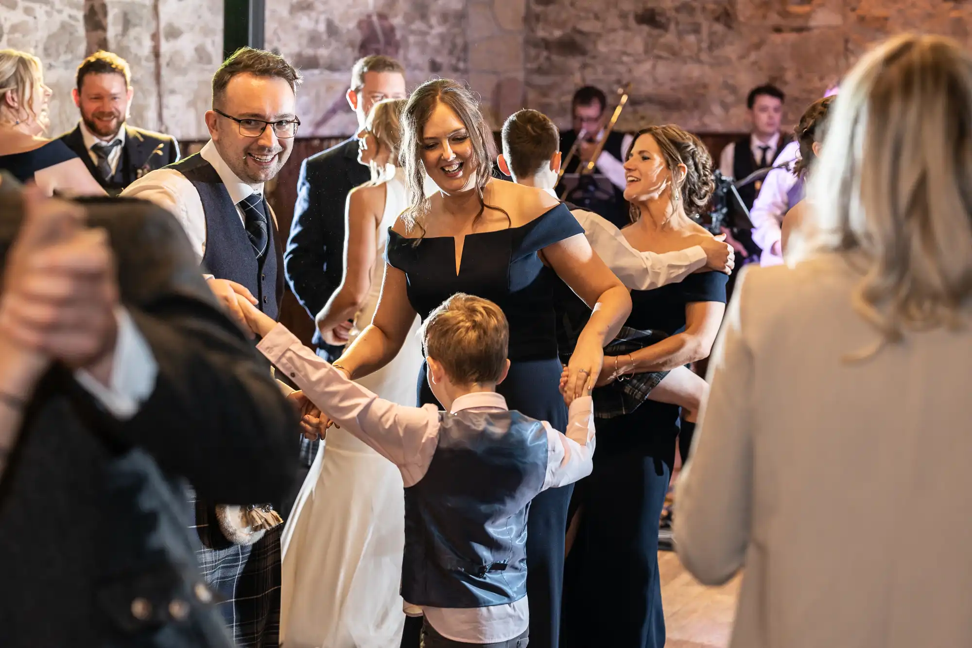 A joyful scene at a wedding reception with guests dancing and smiling, including a couple with a young boy in a formal setting.