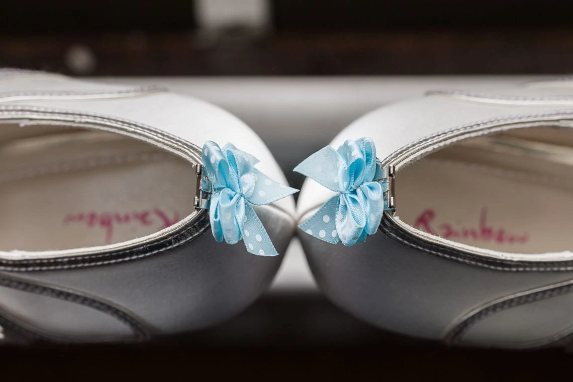 A close-up of white sandals with blue floral bows on the straps, displayed side by side.