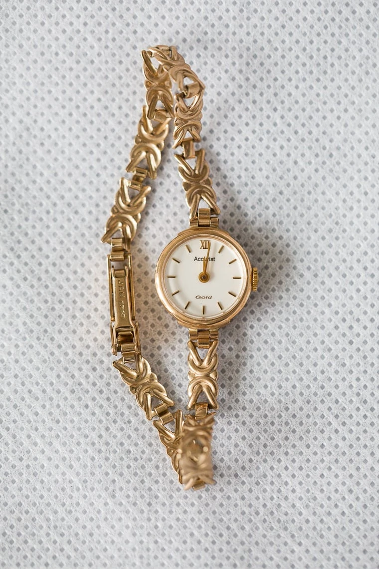 A gold-linked wristwatch with a white dial and roman numerals, displayed on a textured grey background.