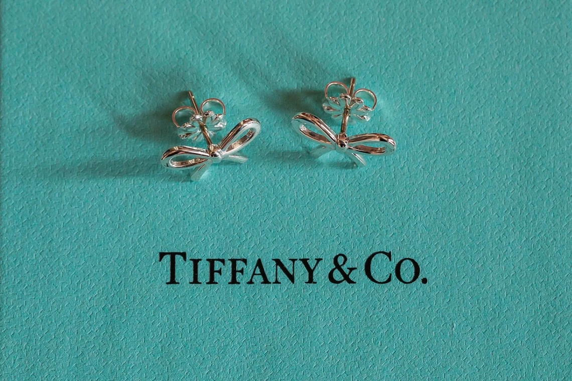 A pair of tiffany & co. silver butterfly earrings displayed on a teal background.