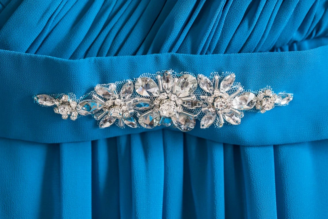 Close-up of a rhinestone and crystal embellished belt on a blue pleated dress.