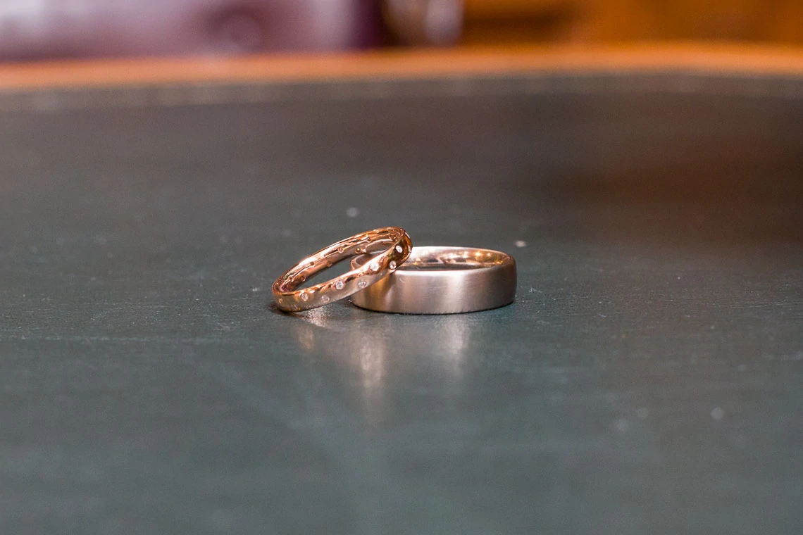Two wedding rings, one plain and one with inset stones, resting on a dark surface.
