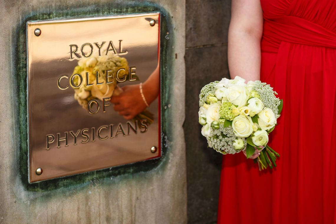 bridesmaid in red dress holding her bouquet next to the brass nameplate of RCPE