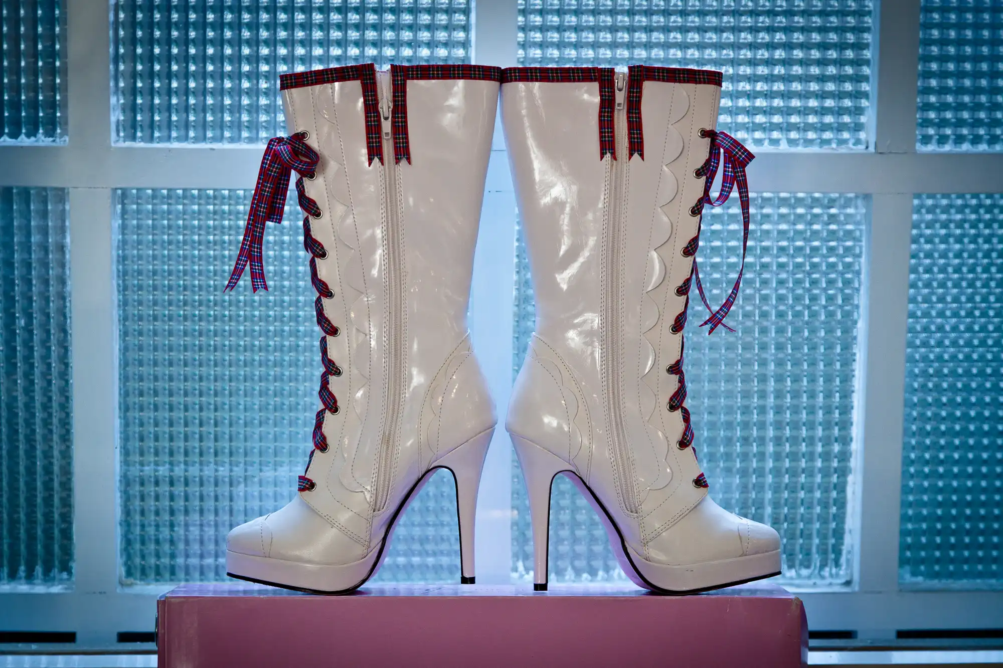 White high-heeled boots with red laces and details, displayed against a translucent blue backdrop.