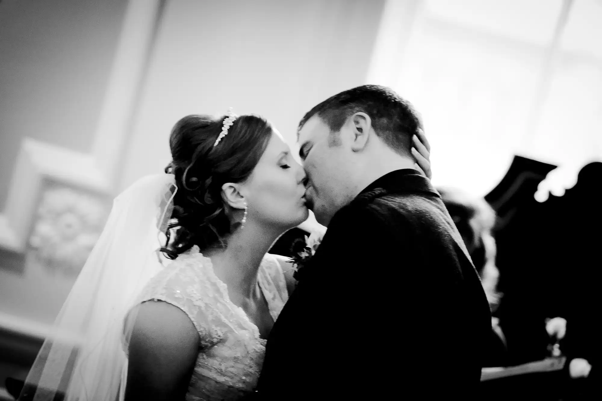 A bride and groom kissing, in black and white, at their wedding ceremony.