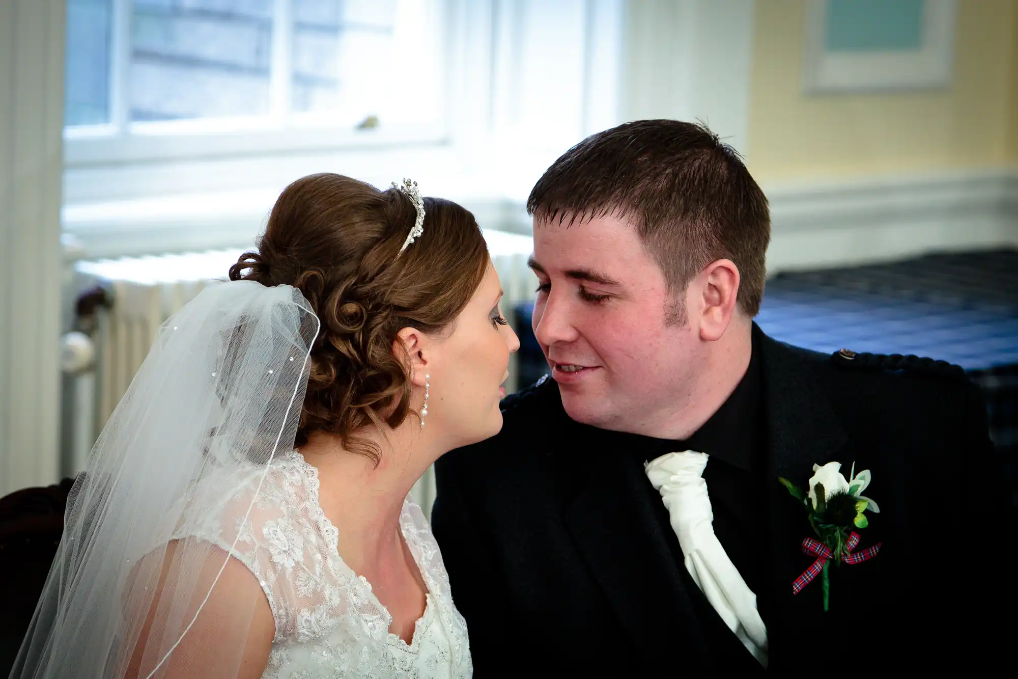A bride and groom in wedding attire, sharing a tender moment, leaning close to each other with joyful expressions.