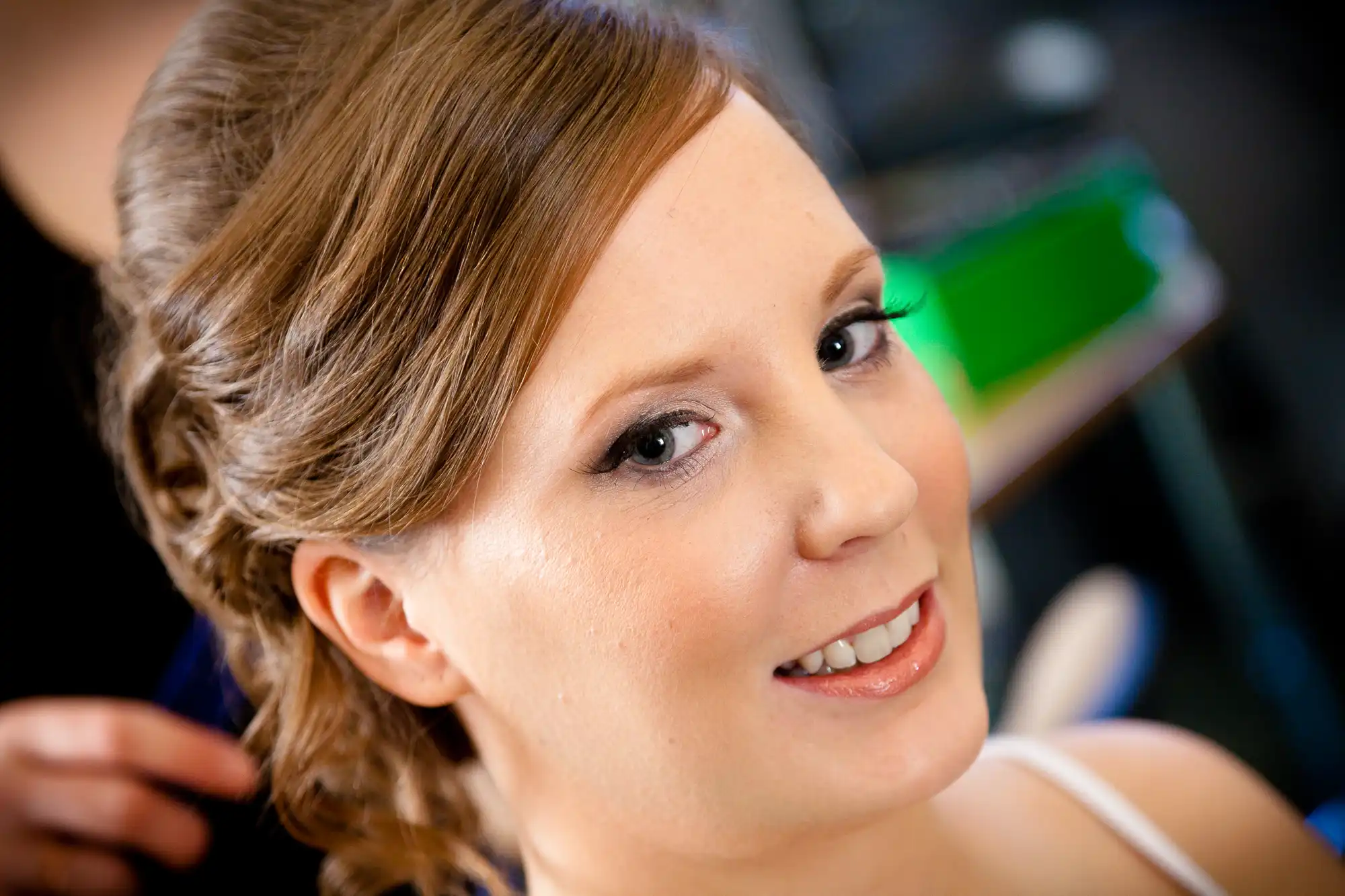 A woman with styled hair and makeup smiling at the camera, in a salon setting with blurred background.