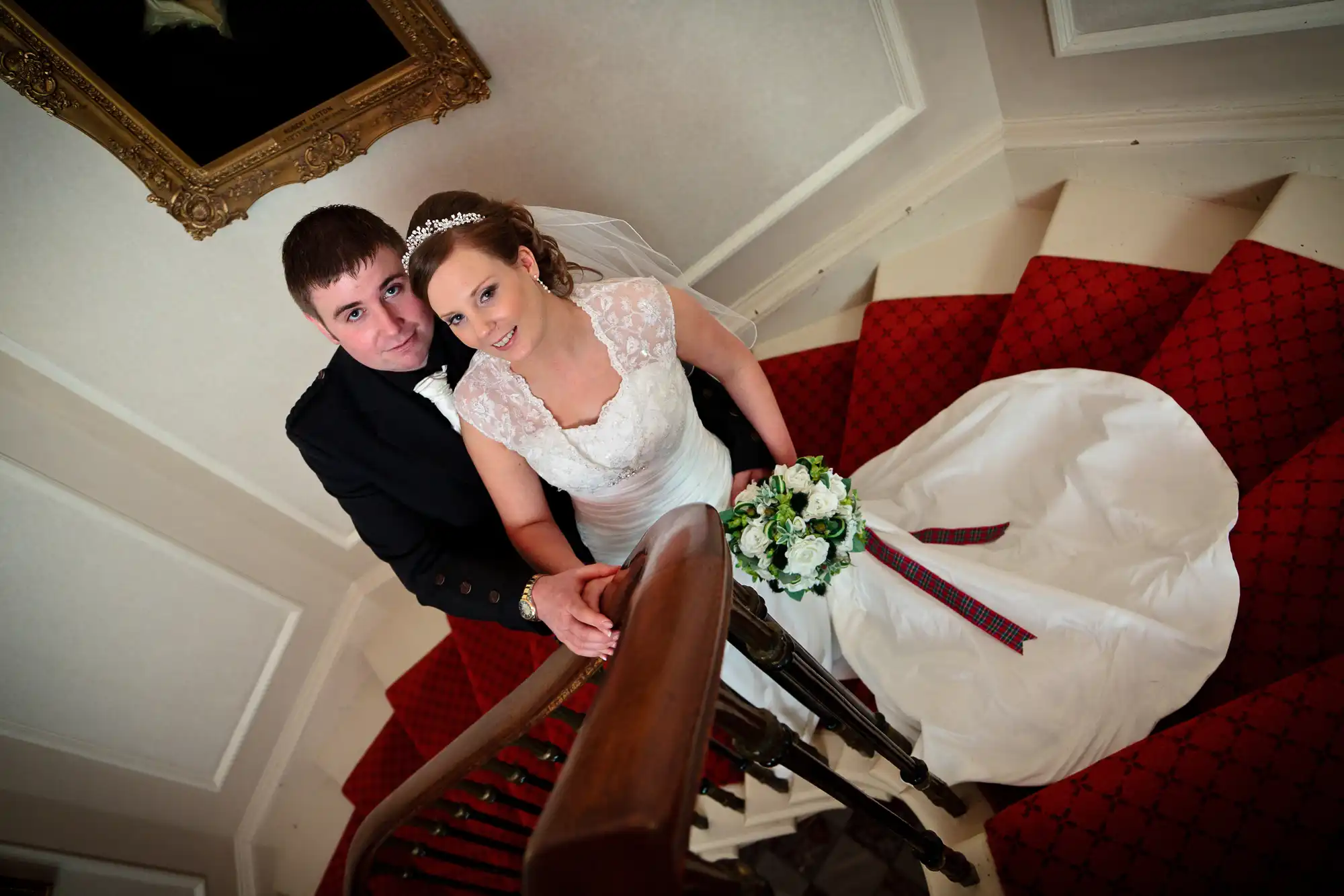 A newlywed couple posing on a staircase, the bride in a white gown and the groom in a dark suit, with a bouquet in hand.