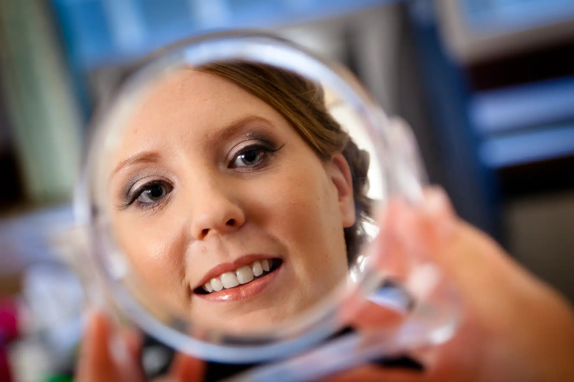 Woman applying makeup, looking into a handheld mirror. the viewpoint is through the mirror, focusing on her face with a blurred background.
