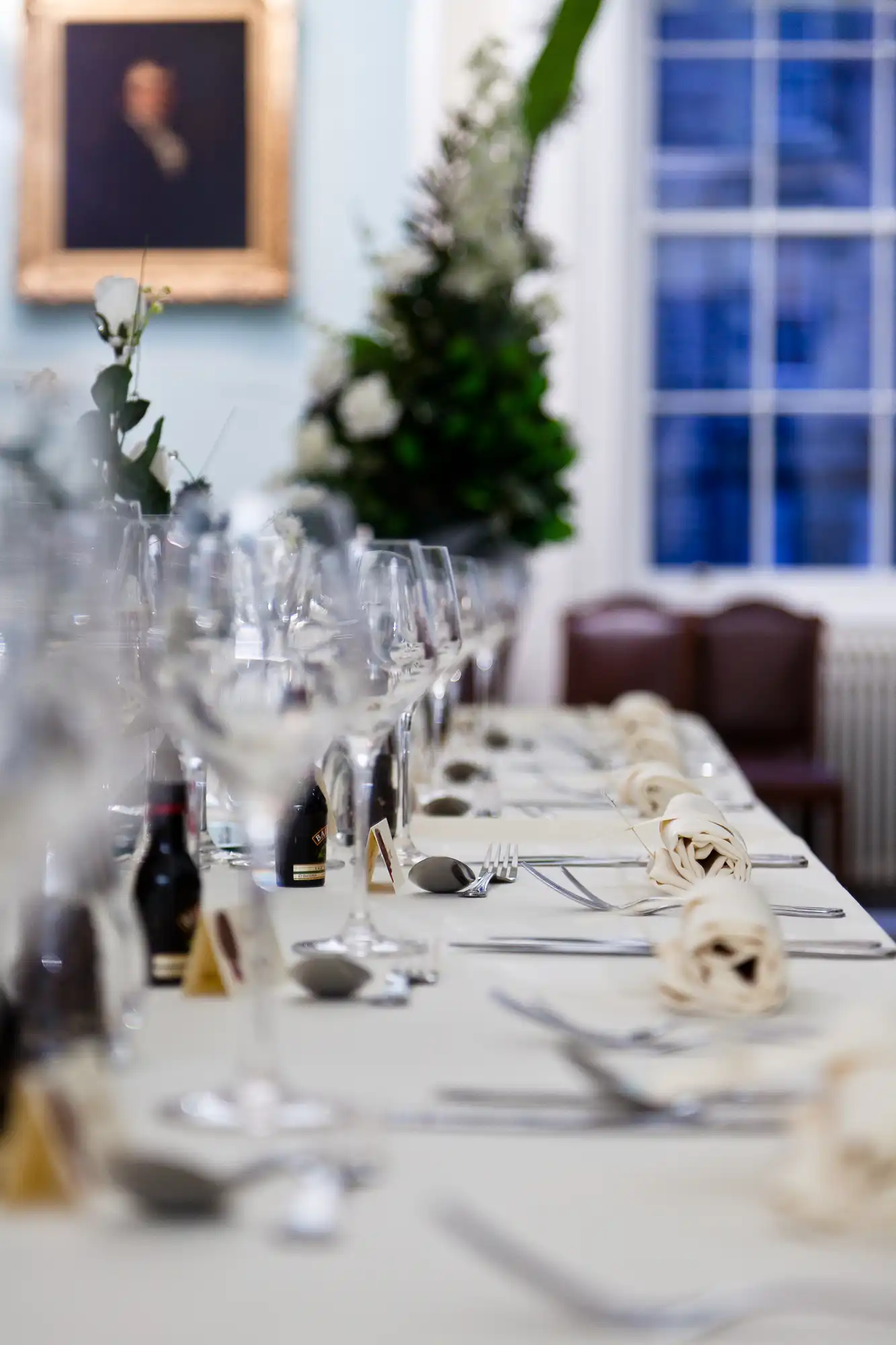 Elegant dining table set for a banquet with wine glasses, plates, and cutlery, featuring a narrow depth of field, with a christmas tree and portrait in the background.