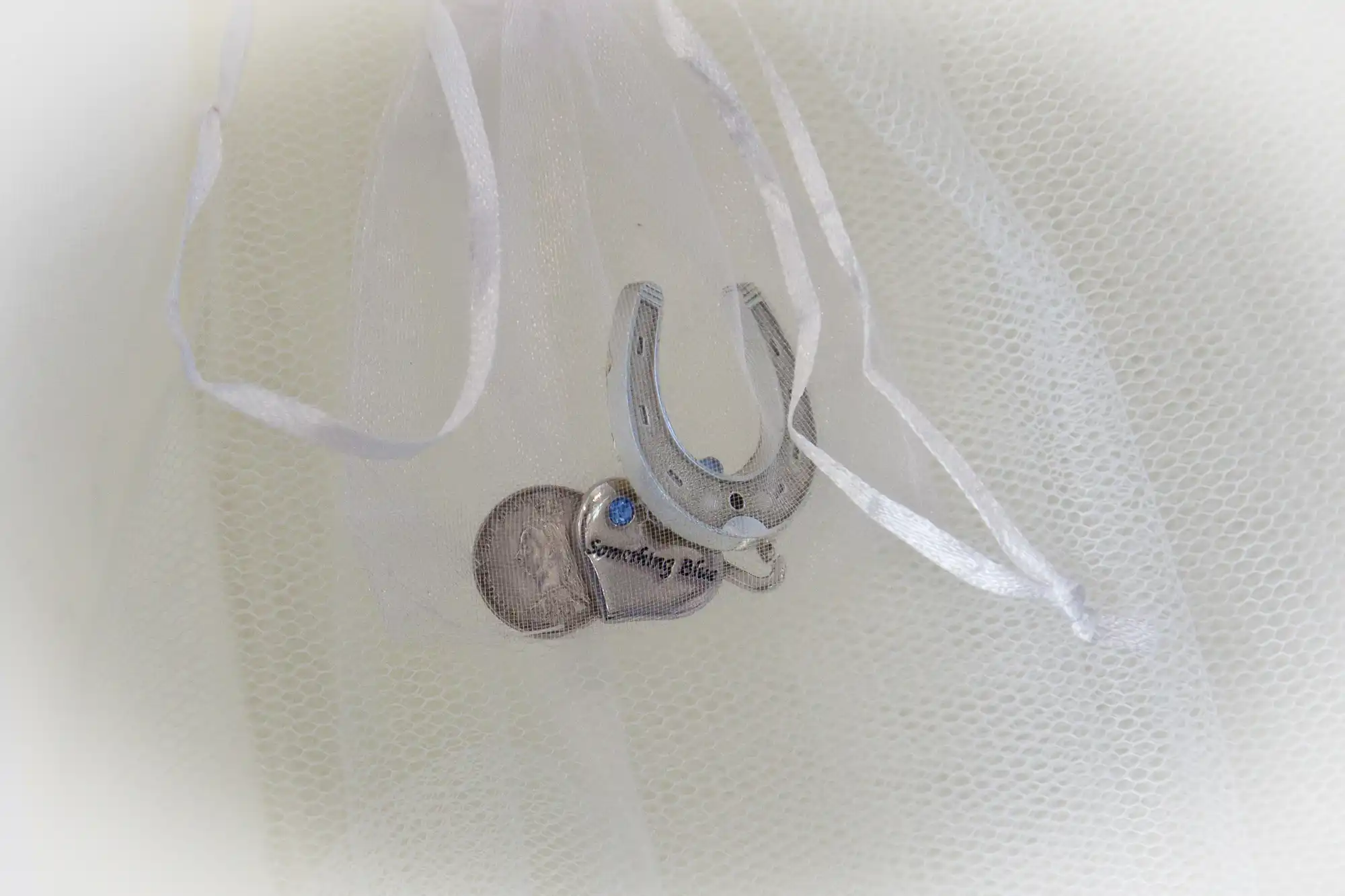 A silver horseshoe and heart charm with "something blue" text, attached to white tulle fabric.