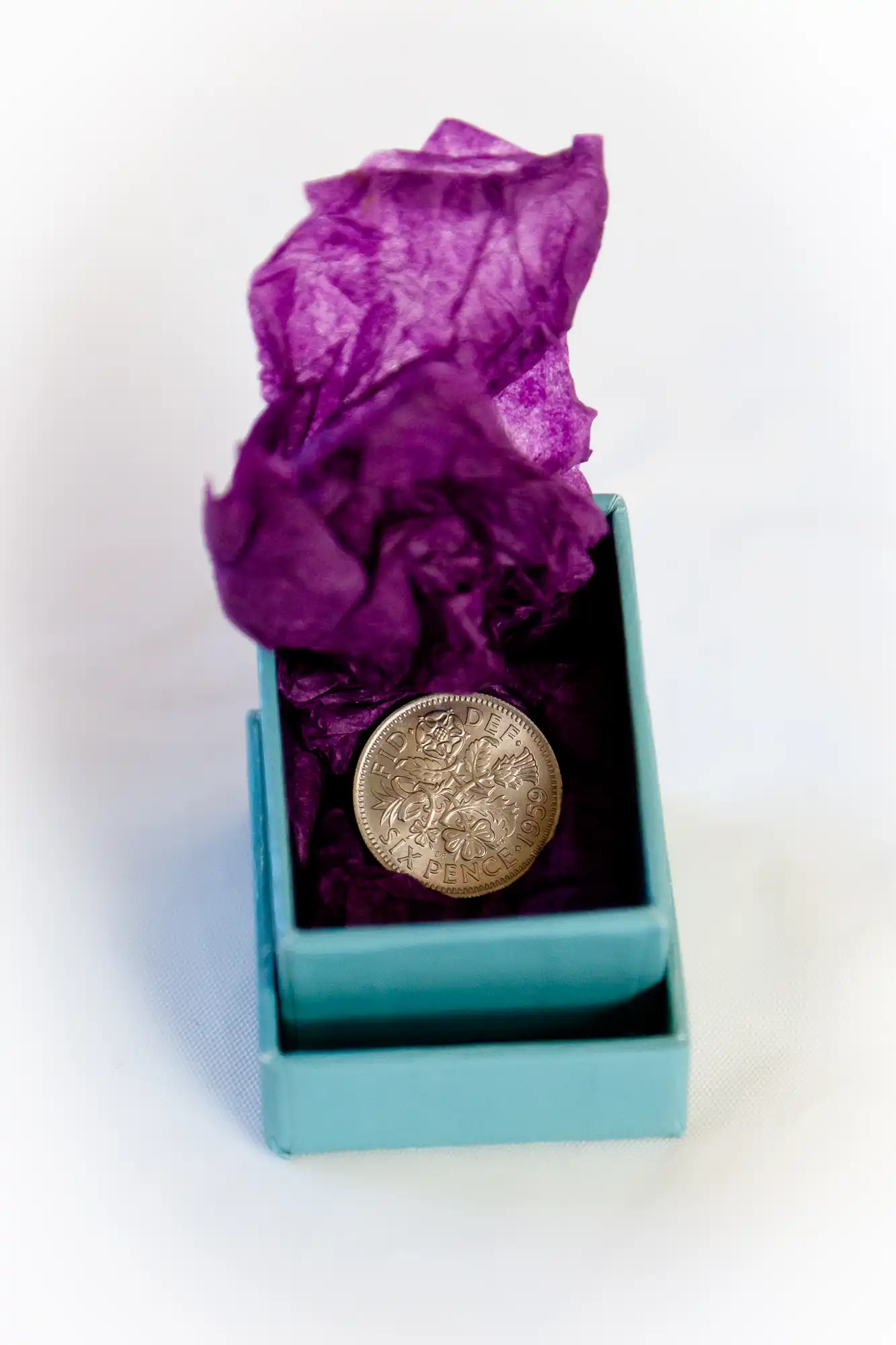 A british one-pound coin rests on purple tissue paper inside a small turquoise gift box.