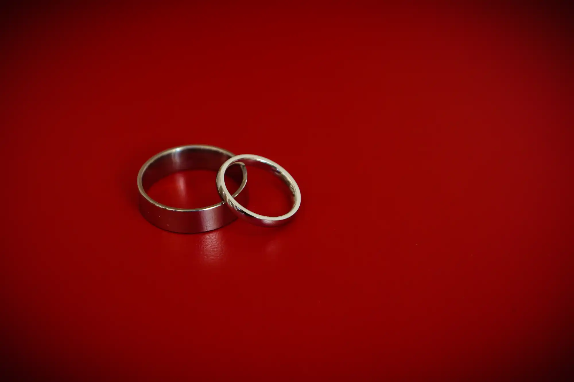 Two silver wedding bands lying on a red background.