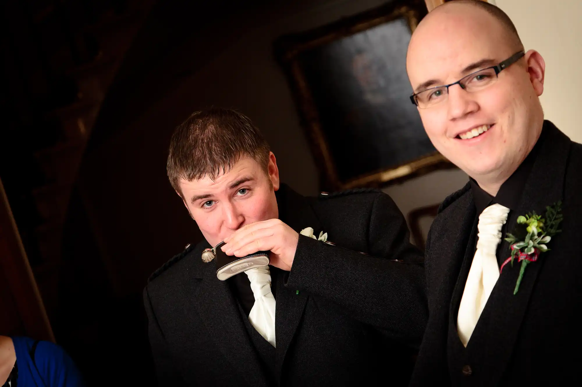 A man in a dark military uniform kisses the hand of his partner, likely during a wedding, while another man in a black tuxedo smiles at the camera.