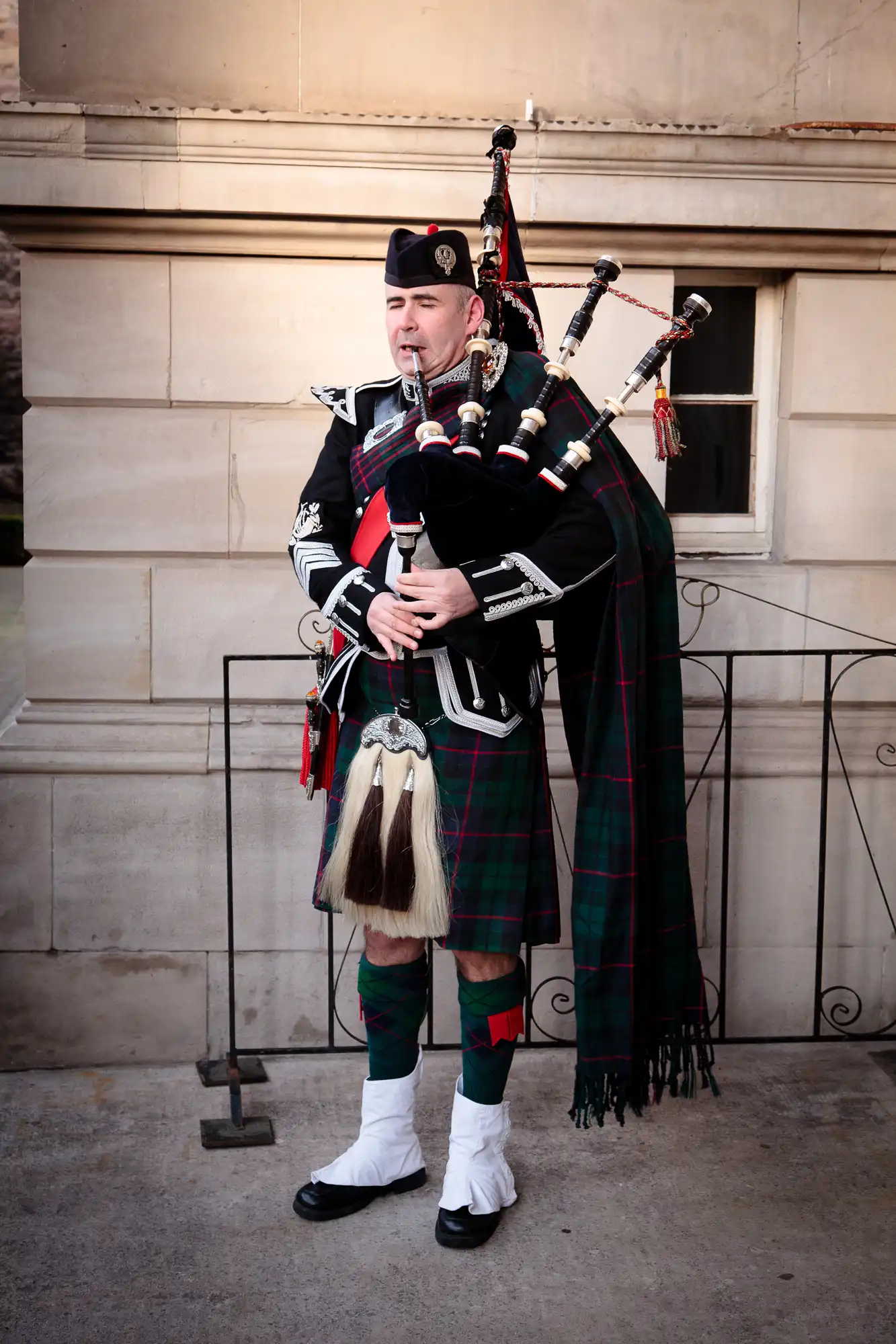 A man in traditional scottish highland dress playing the bagpipes, featuring a tartan kilt and a sporran.