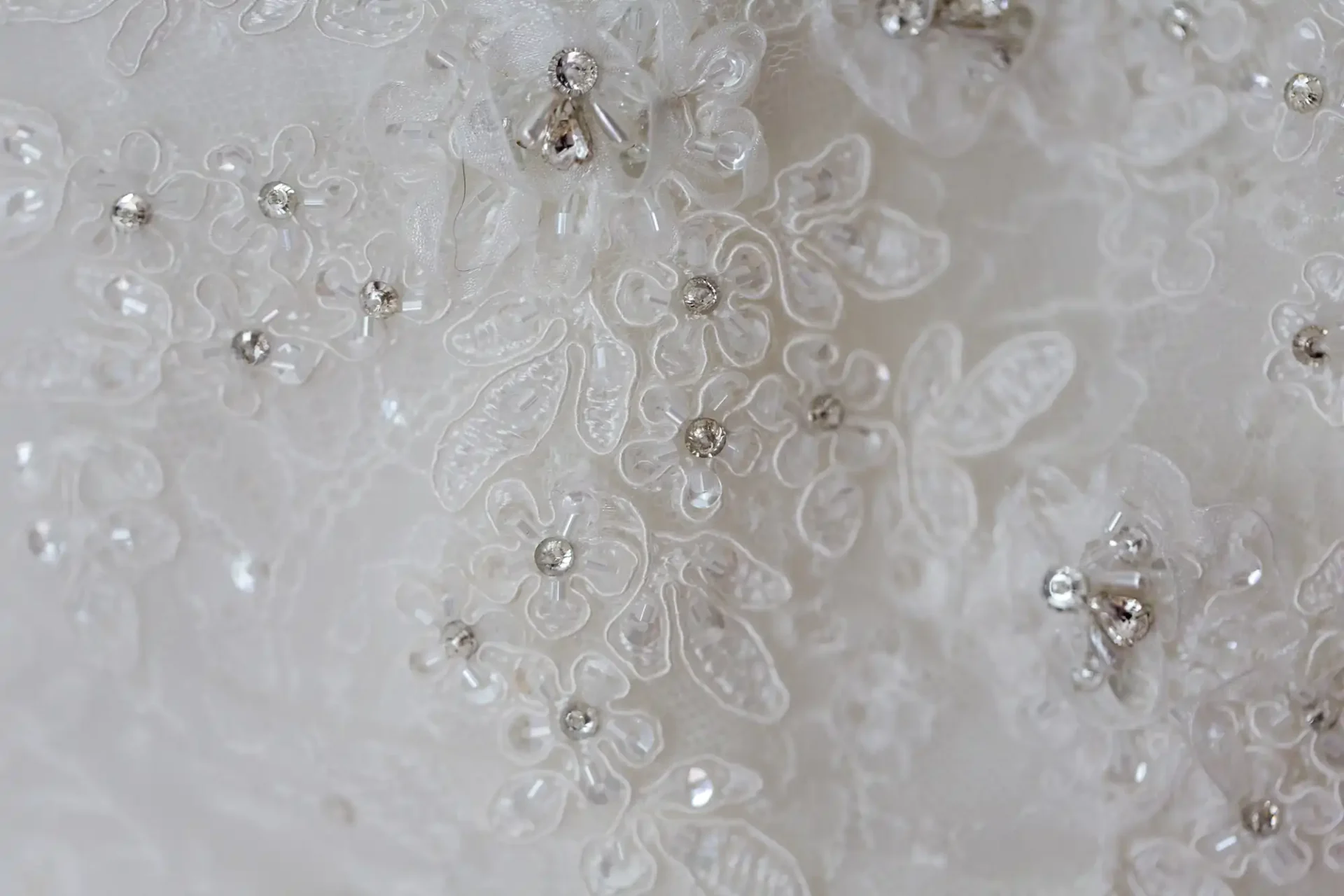 Close-up of a white wedding dress featuring detailed floral embroidery with small beads and sequins.