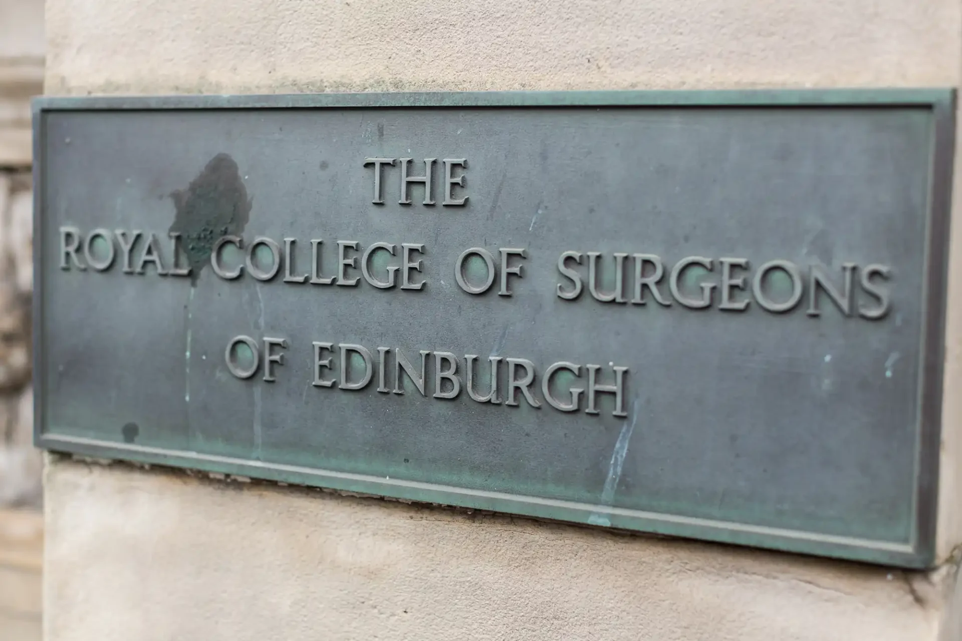 Bronze plaque reading "the royal college of surgeons of edinburgh" on a stone wall, with slight wear marks.