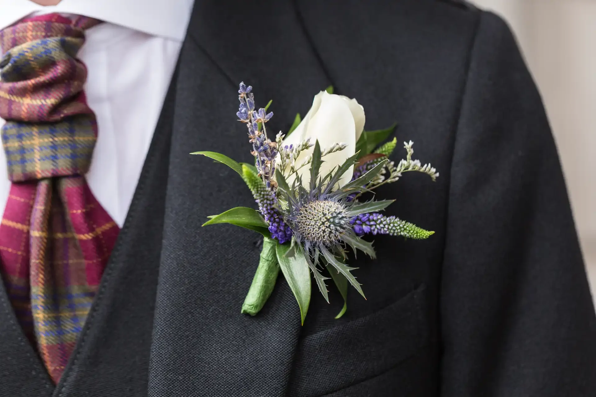 Close-up of a groom's dark suit with a white rose and lavender boutonniere, complemented by a vibrant, striped tie.