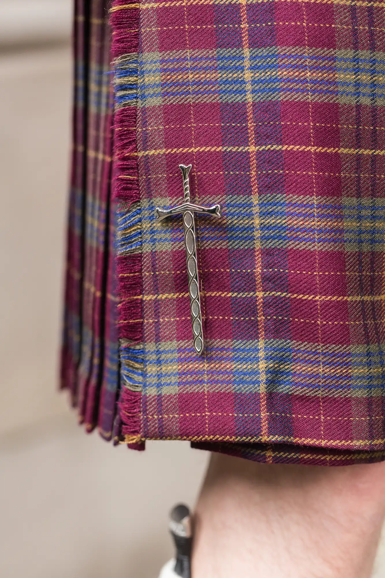 Close-up of a tartan kilt with a decorative silver sword pin attached to the fabric.