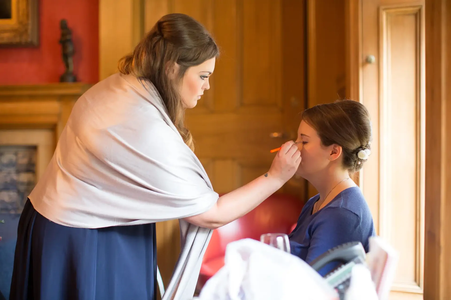 A woman applying makeup to a young girl in an elegantly furnished room.