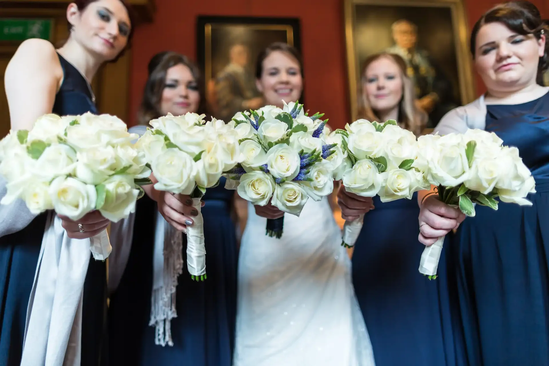 A bride and her bridesmaids in navy dresses posing with white and blue bouquet flowers, focused on the bouquets.