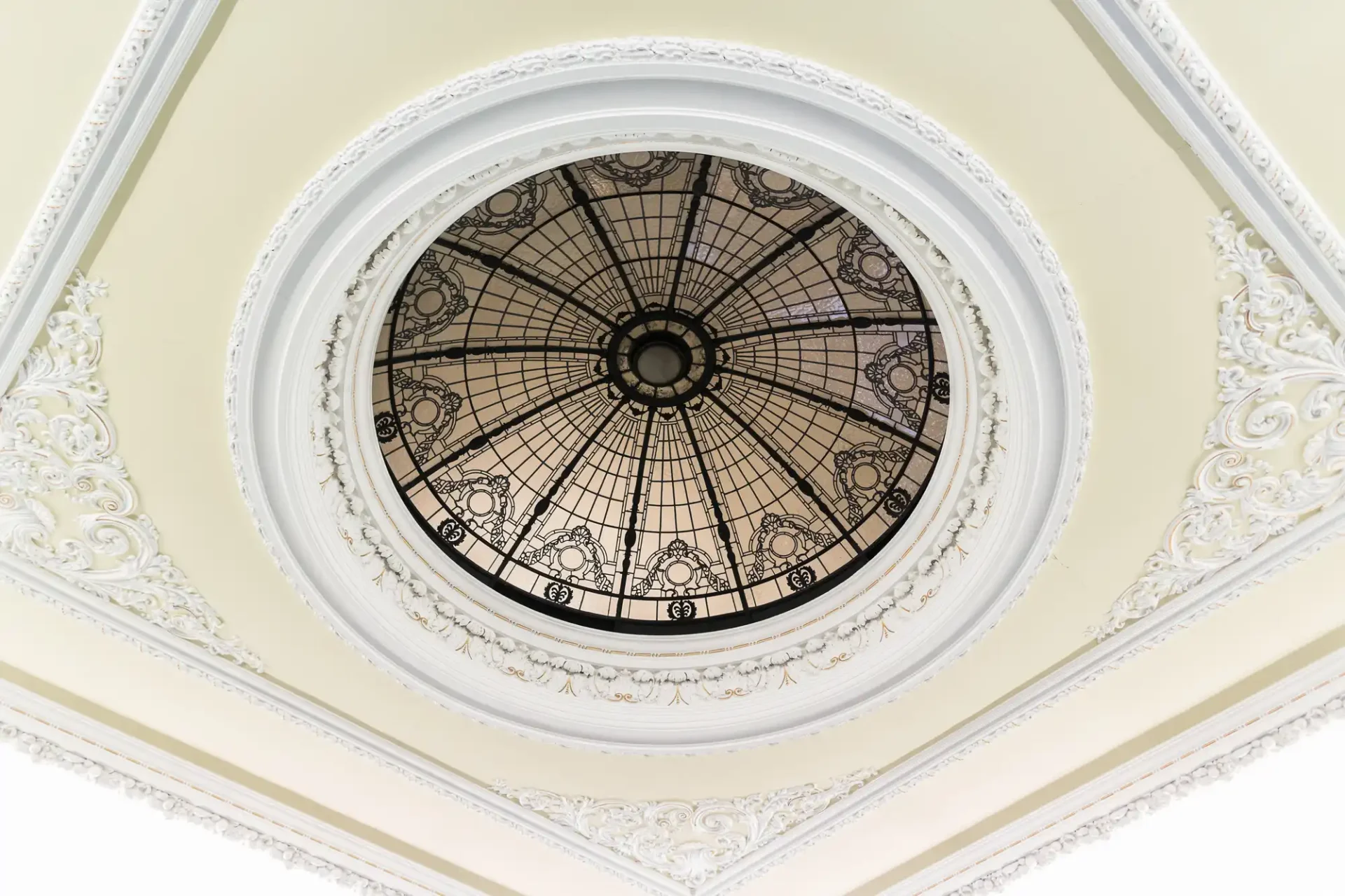 Ornate domed skylight with intricate metal framework set in an elaborately detailed white ceiling.