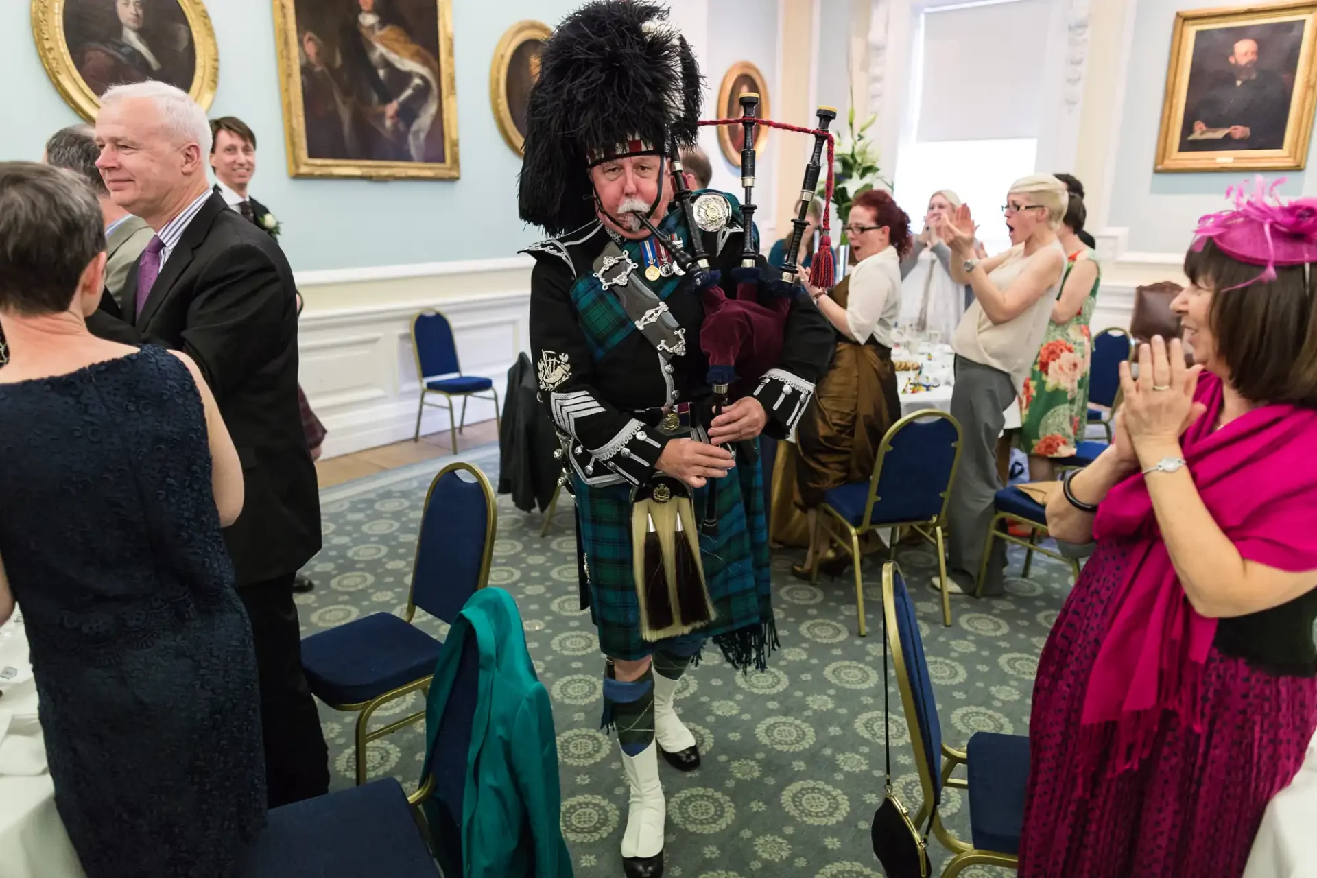 A bagpiper in traditional scottish attire playing at a formal indoor gathering with applauding guests.