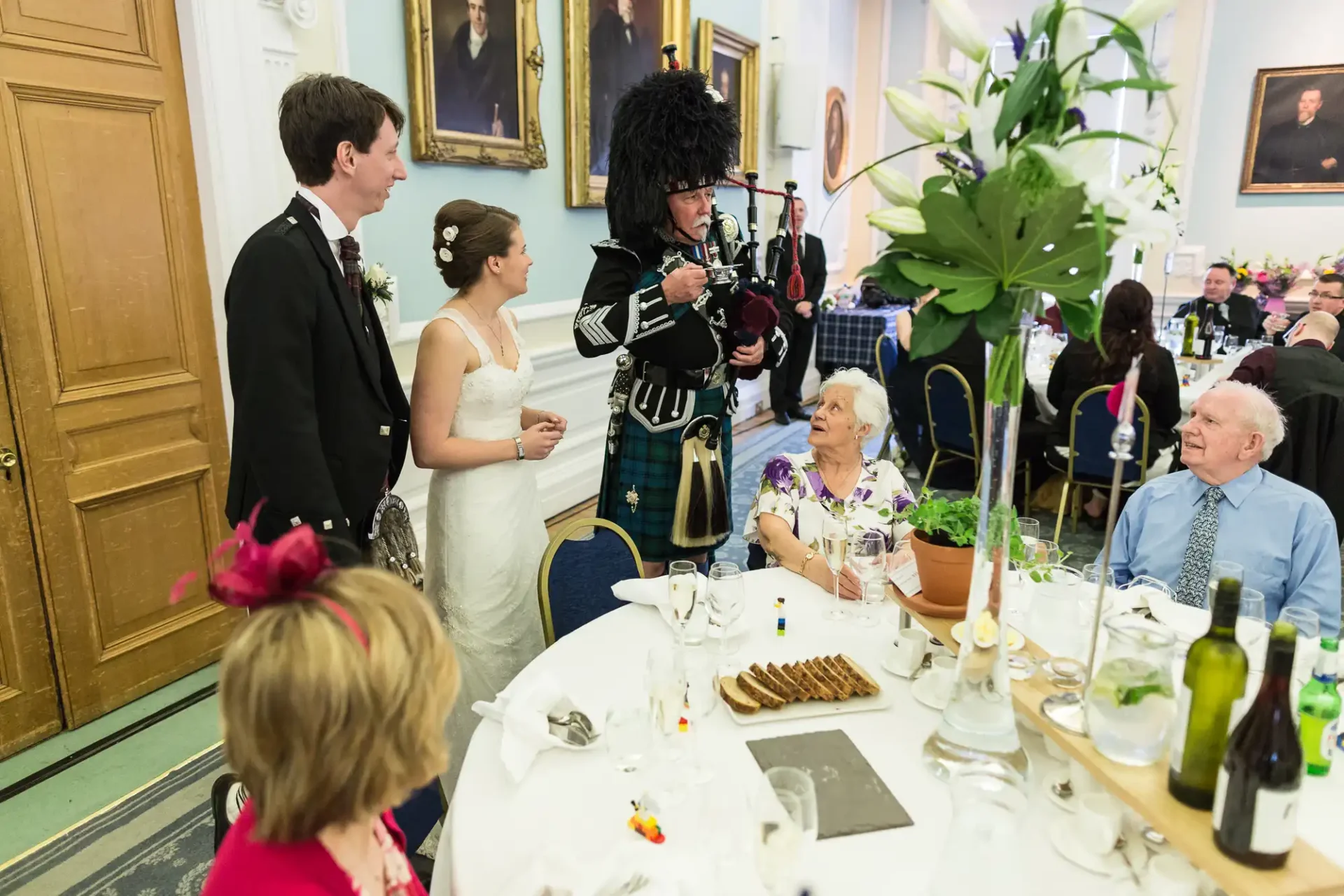 A bagpiper in traditional scottish attire performing at a wedding reception with guests watching.