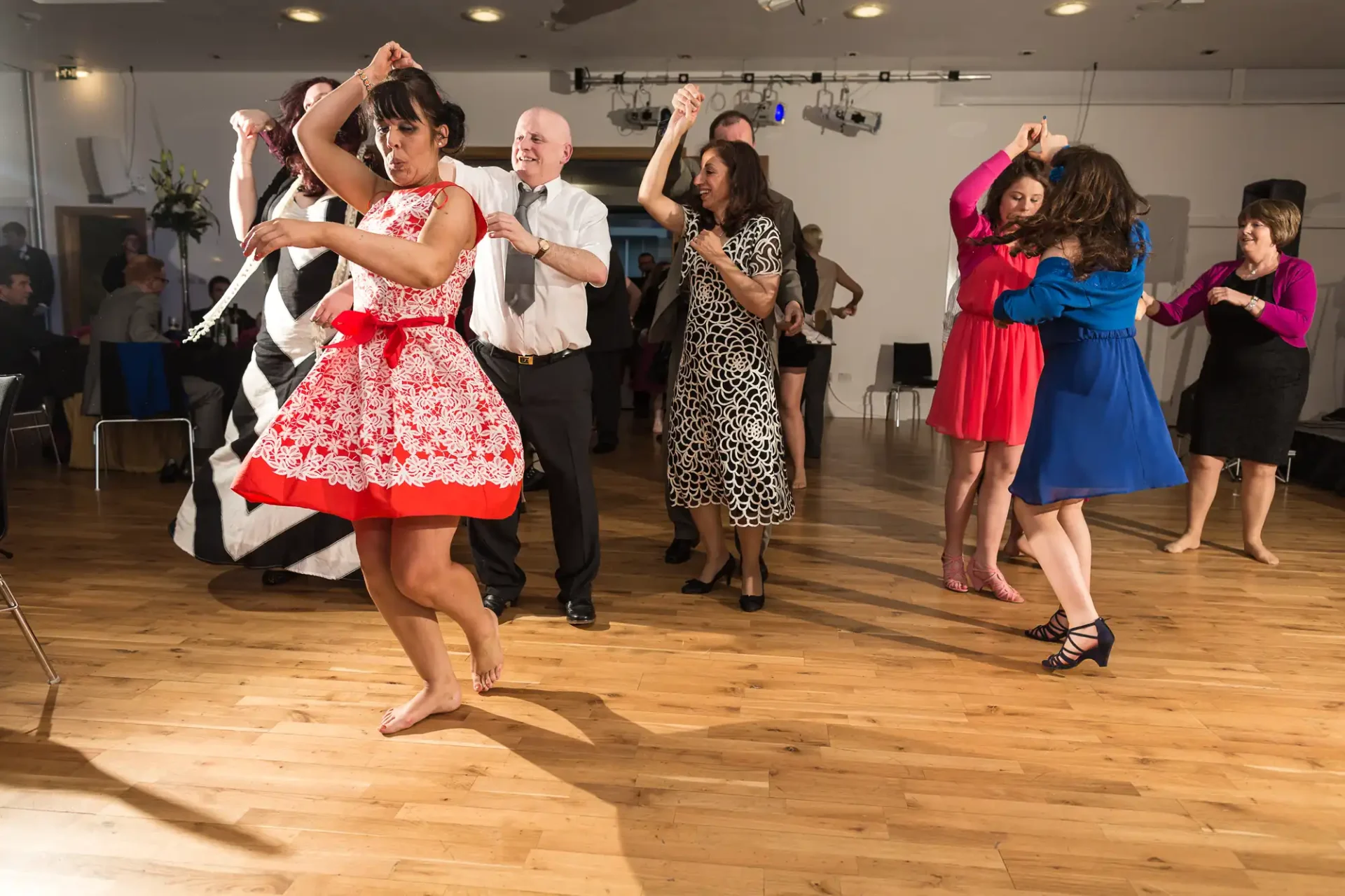 Adults dancing together at a lively event, with some couples performing dance moves while others enjoy in the background.