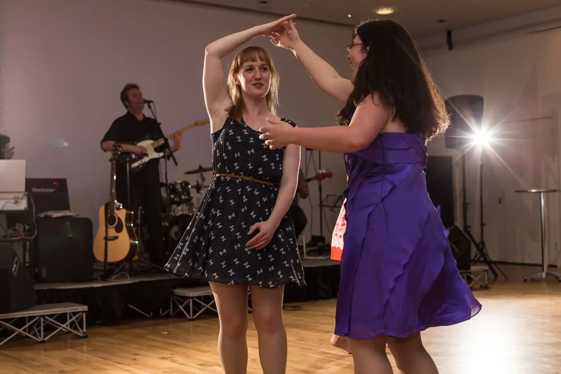 Two women dancing and smiling at each other in a ballroom with a live band playing in the background.