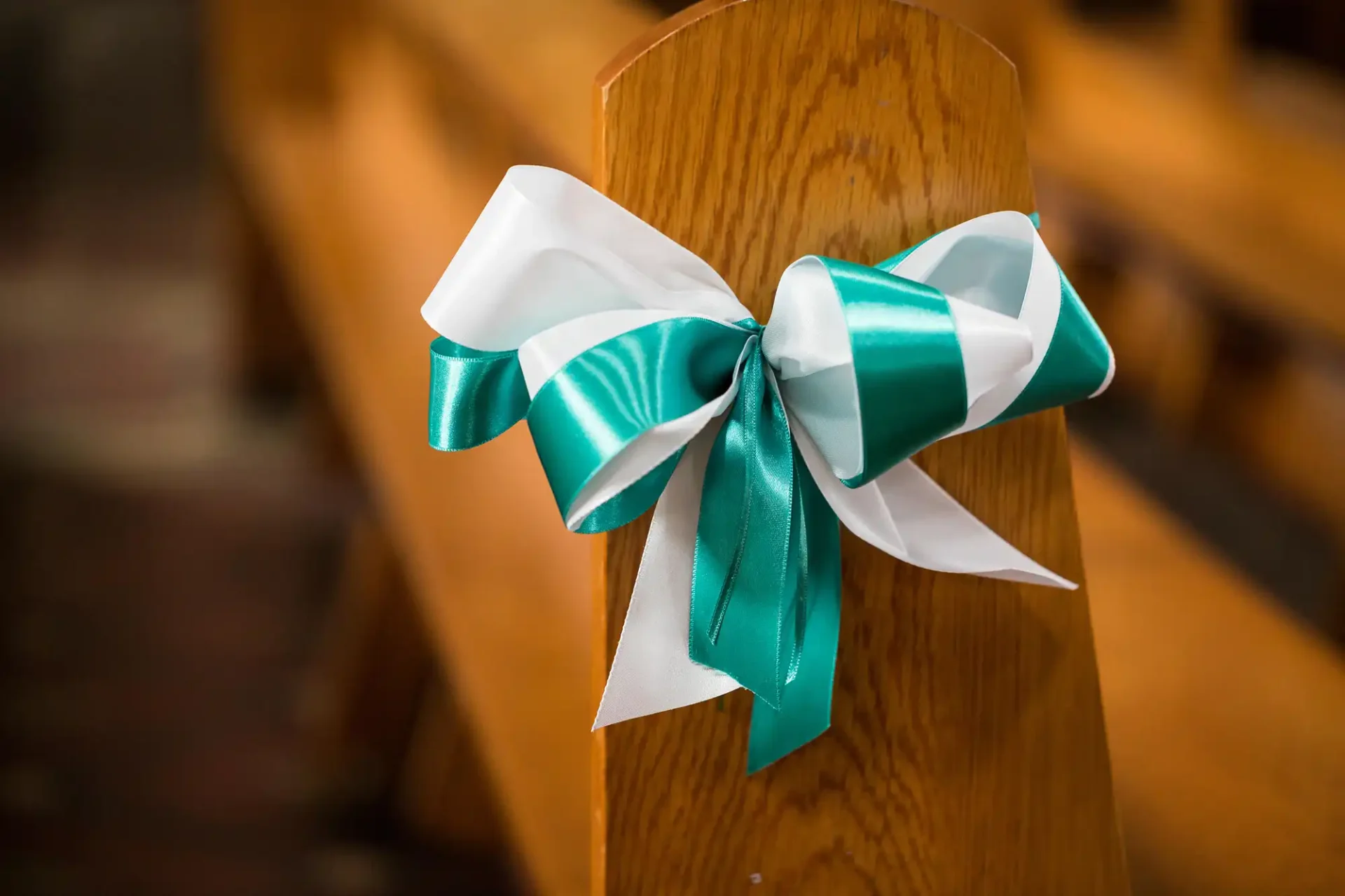 A teal and white ribbon bow tied around a wooden church pew.