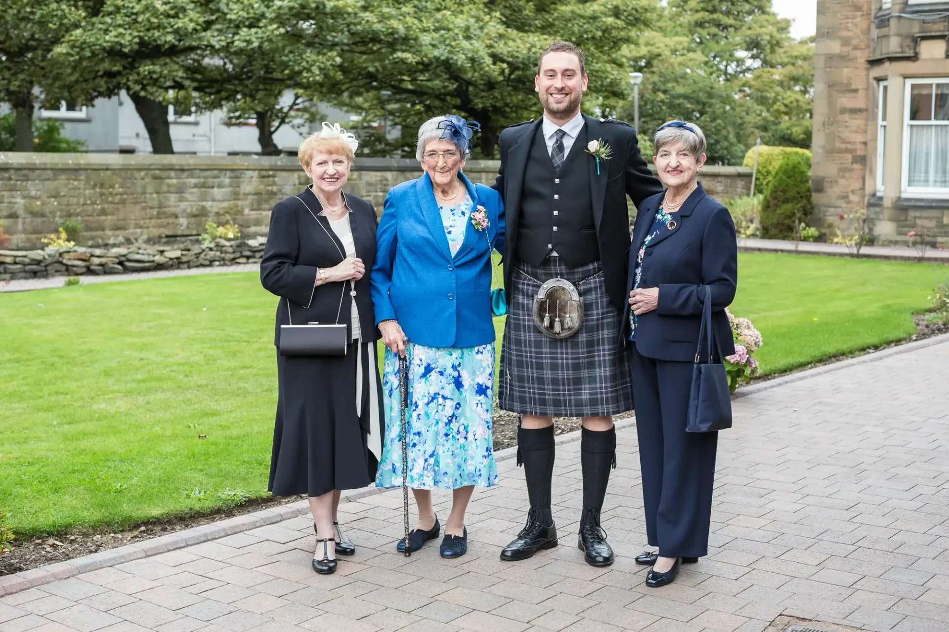 Four people in formal attire, including a man in a kilt, posing together at an outdoor event.