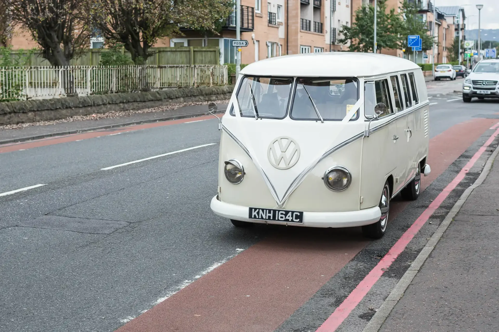 A vintage cream-colored volkswagen bus parked on a city street, with buildings in the background.