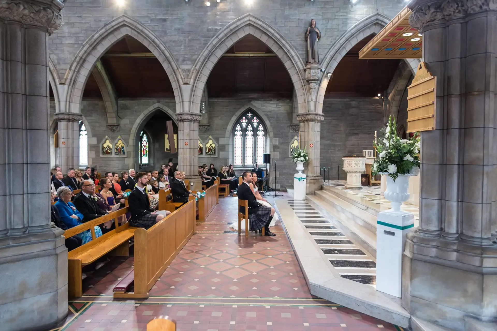 People attending a service inside a spacious church with stone arches and stained glass windows.