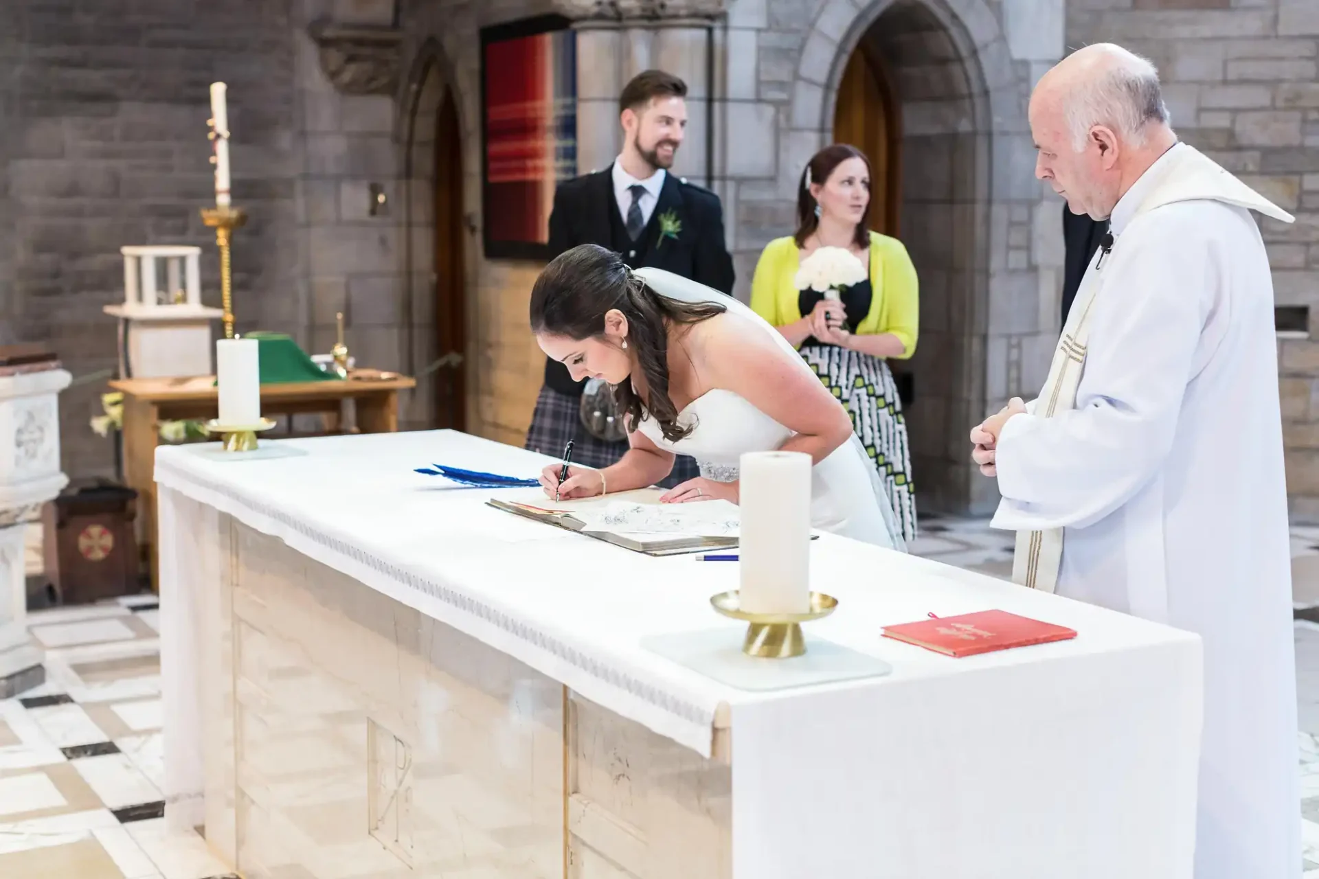A bride signs a marriage document at a church altar, watched by a priest and a couple standing in the background.