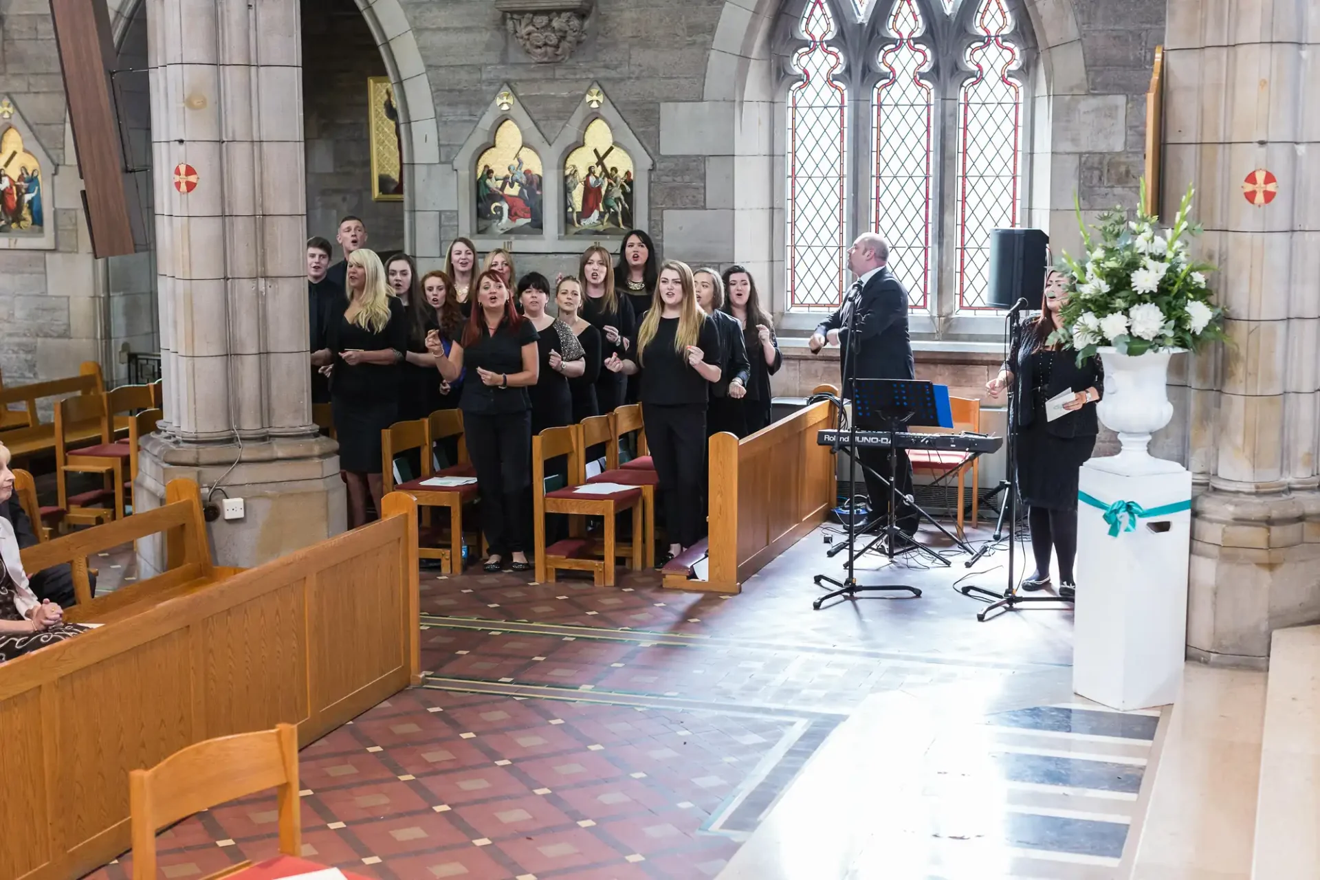 A choir performing in a church, accompanied by a conductor and a musician with a keyboard.
