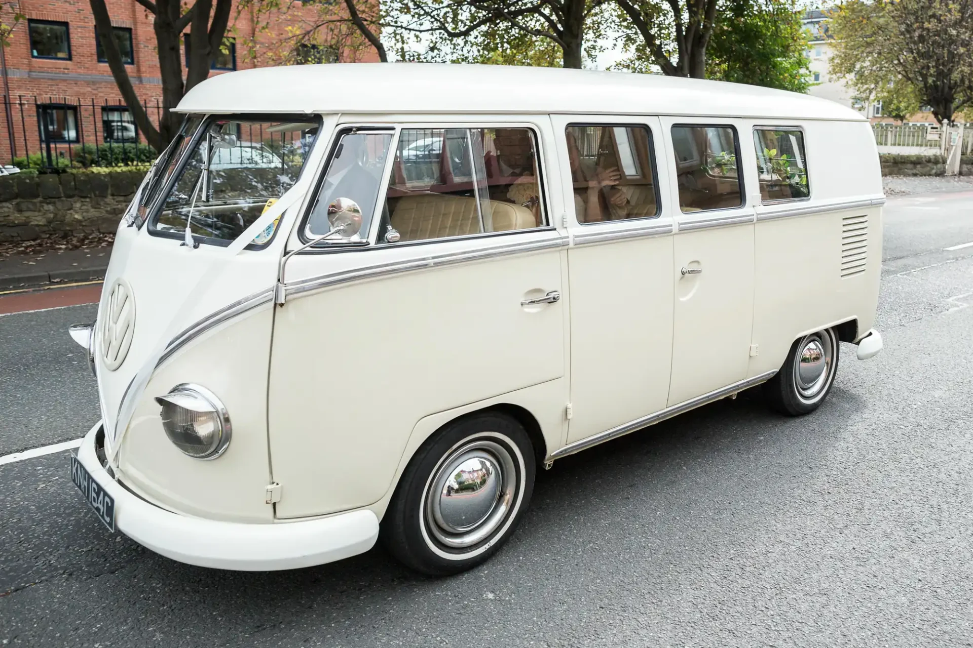 A vintage cream-colored volkswagen bus parked on a street, with a driver visible inside.
