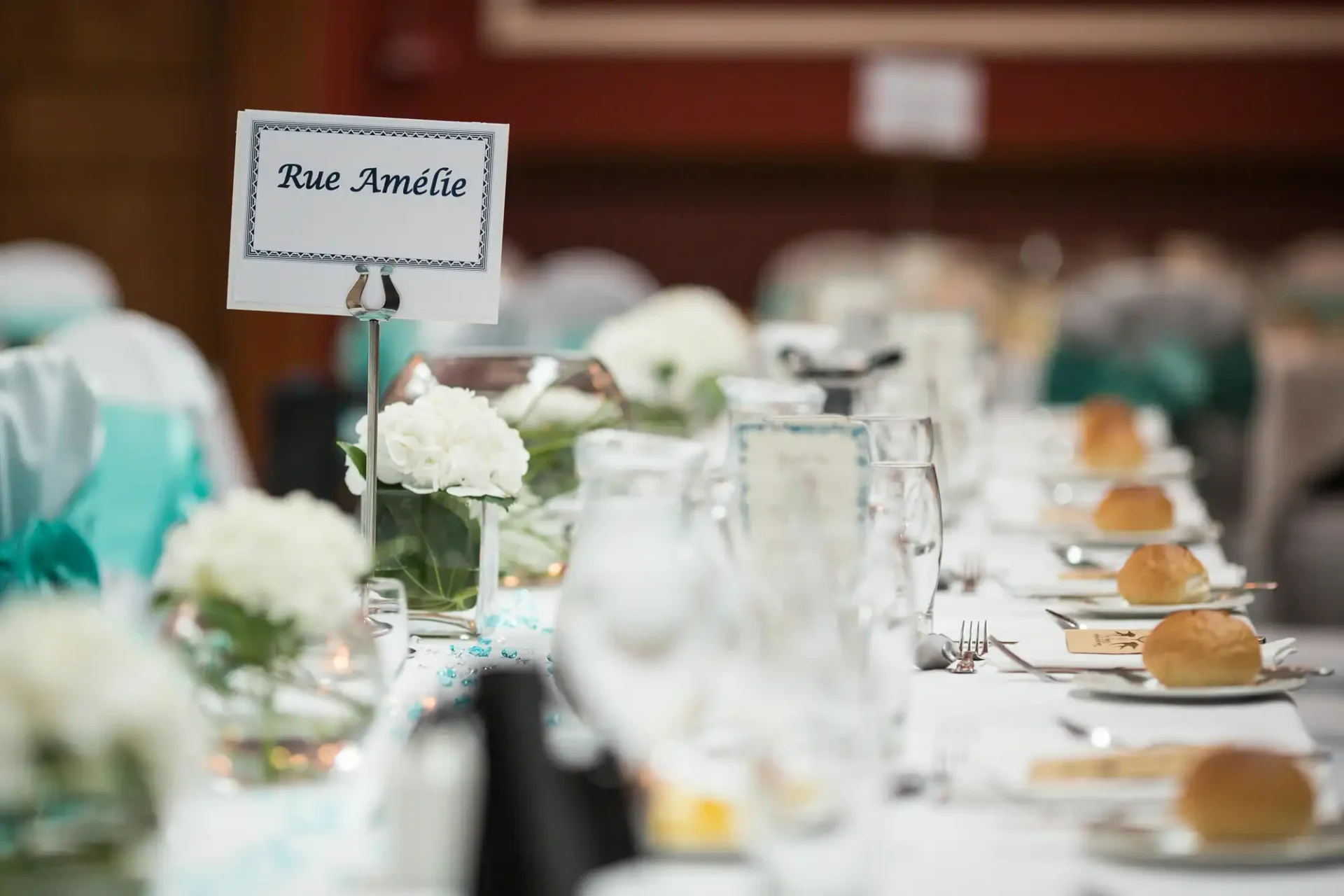 An elegantly set banquet table with white flowers and a sign reading "rue amélie" at a dinner event.