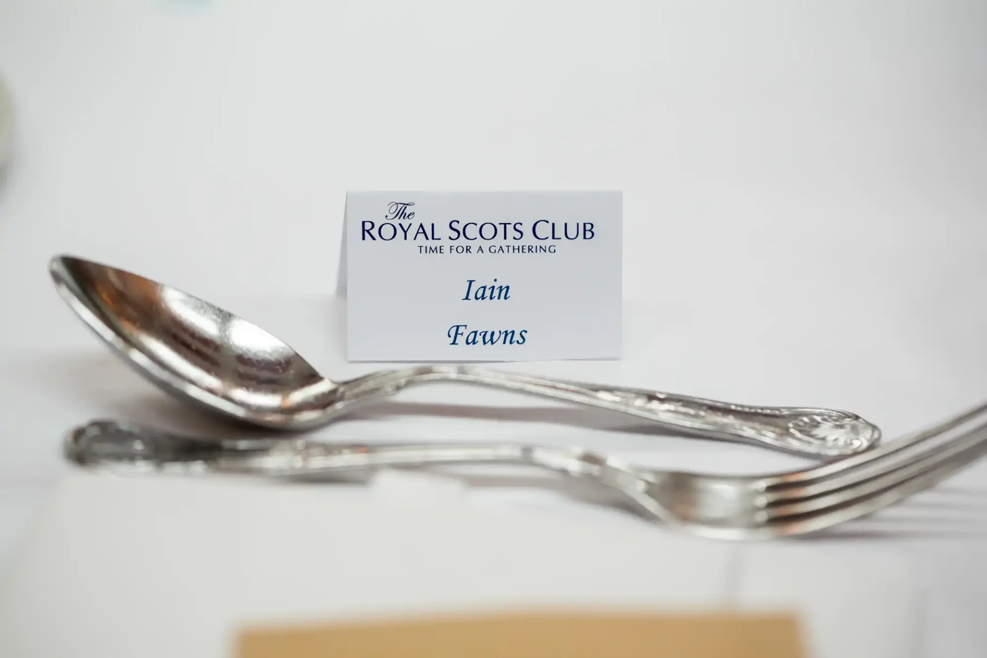 Place setting with a spoon, fork, and a name card reading "iain fawns" for the royal scots club event.