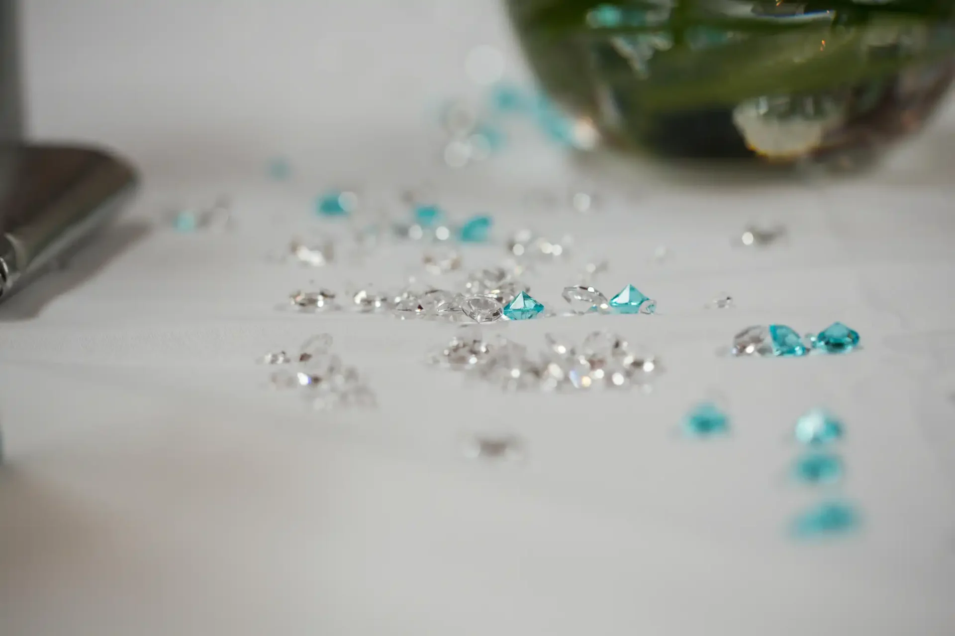 Scattered clear and turquoise gemstones on a white tablecloth with a blurred background.
